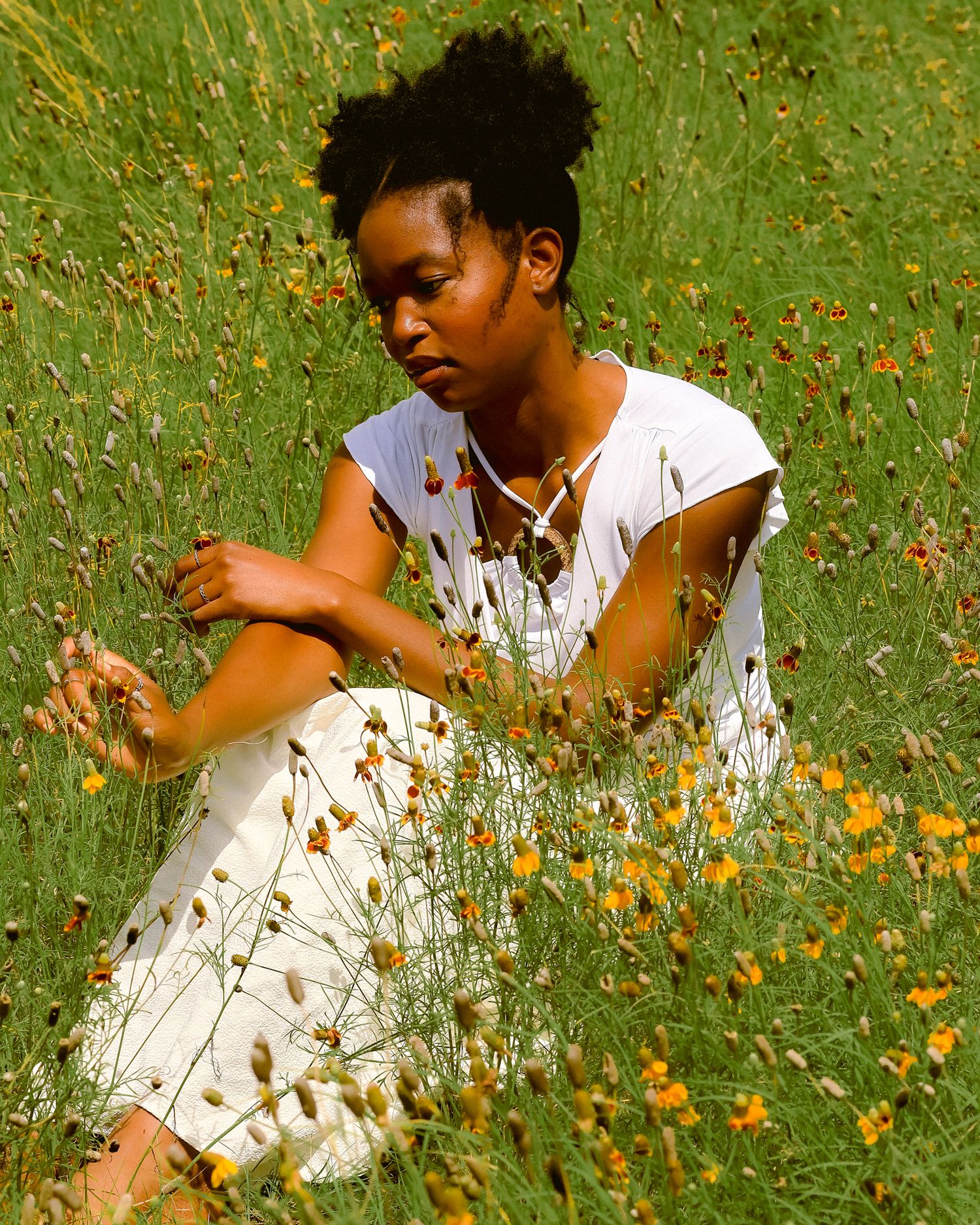 Artistic photo of person sitting among yellow wildflowers in white dress.