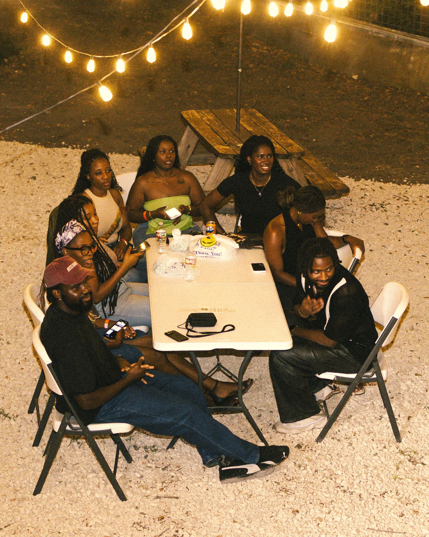 Group seated around a white table under string lights at an outdoor social event.