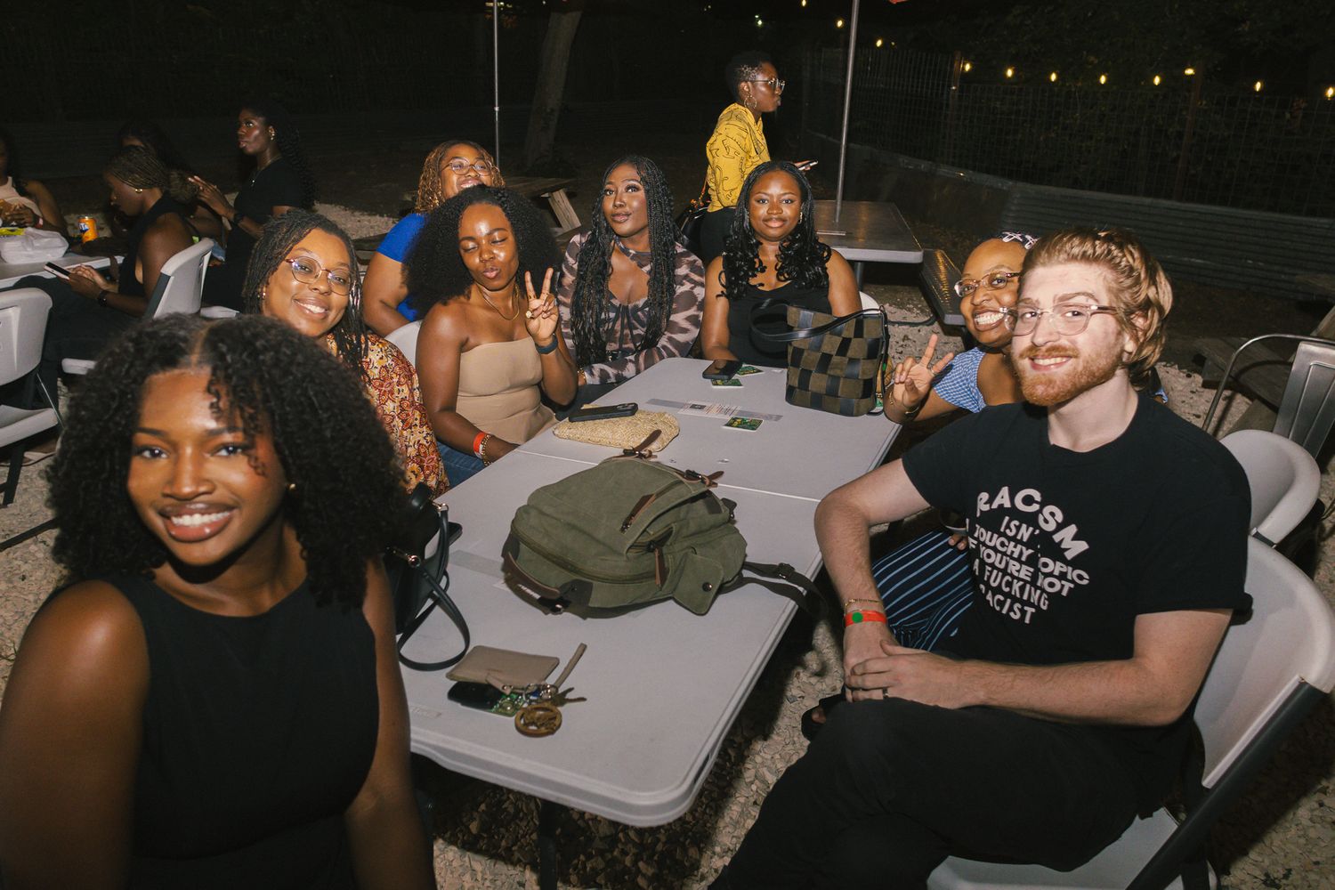 Evening social gathering with people seated at tables under ambient outdoor lighting.