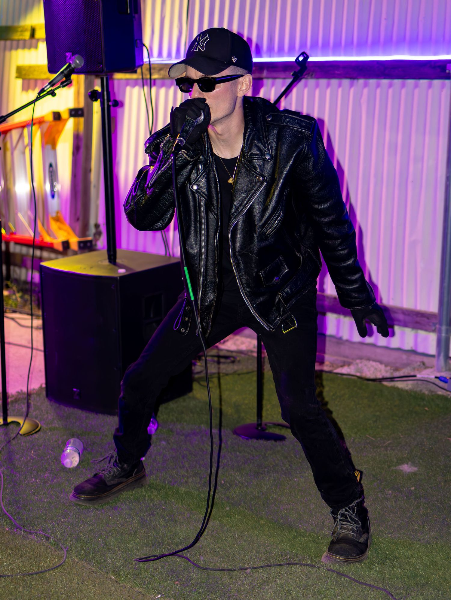 Dynamic stage performance with figure in black leather and cap under colorful venue lighting.