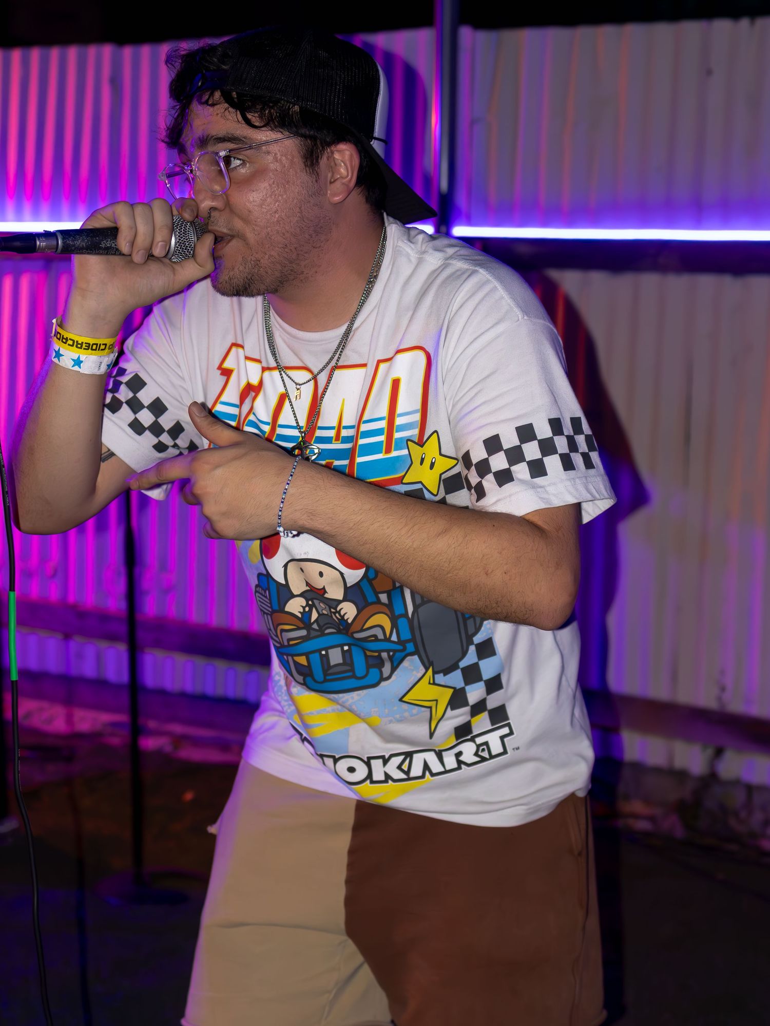 Performer in Nintendo themed t-shirt singing into microphone under colorful stage lighting.