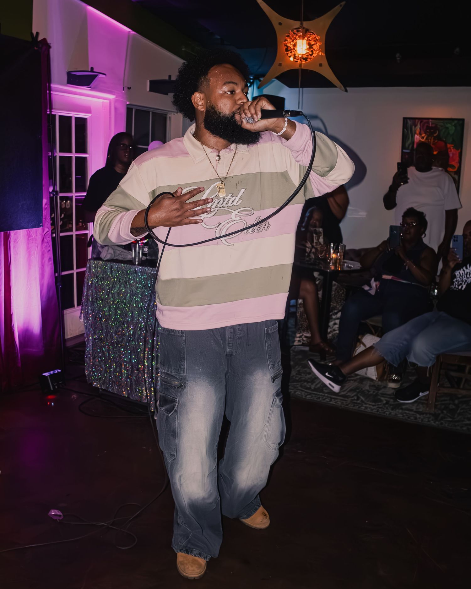 Performer in white shirt and jeans singing on stage with purple lighting in a small venue.