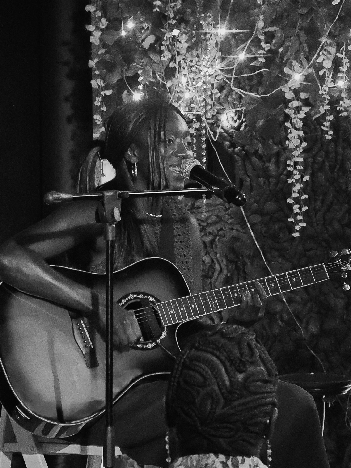 Black and white view of acoustic guitar setup with decorative lighting and floral elements on stage.
