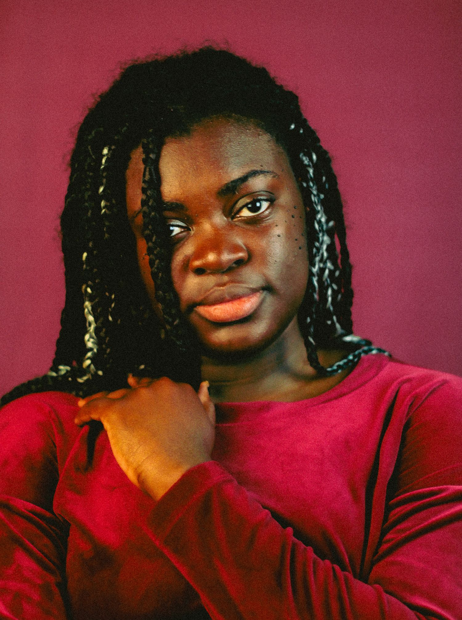 Young woman with braided hair in a red velvet top poses thoughtfully against a deep red studio background.