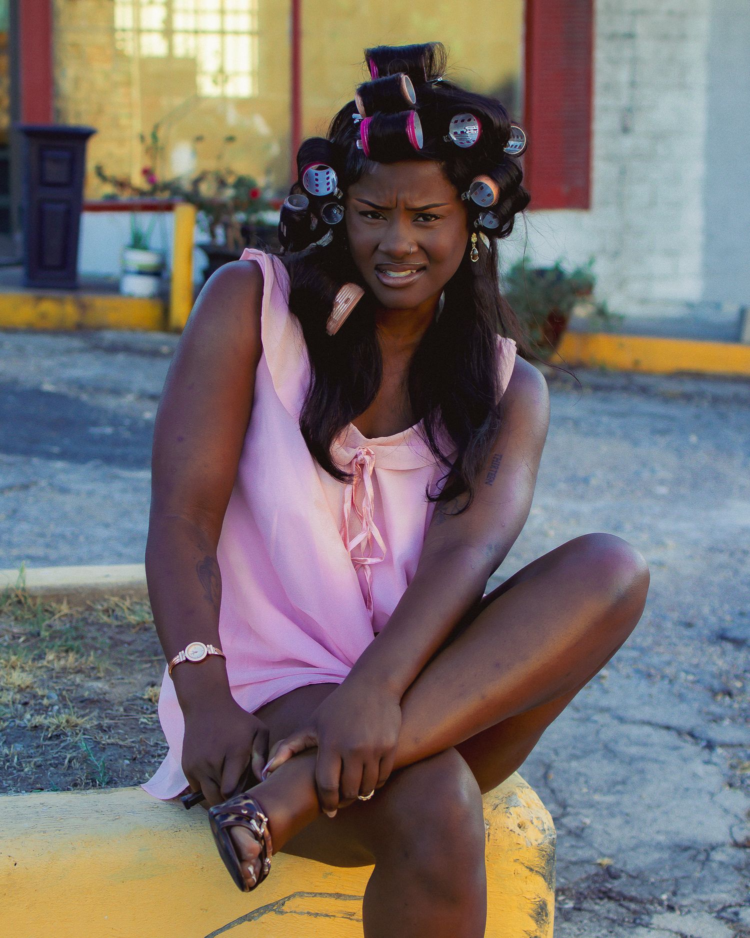 Casual outdoor portrait session showing someone seated wearing a pink top and hair rollers.