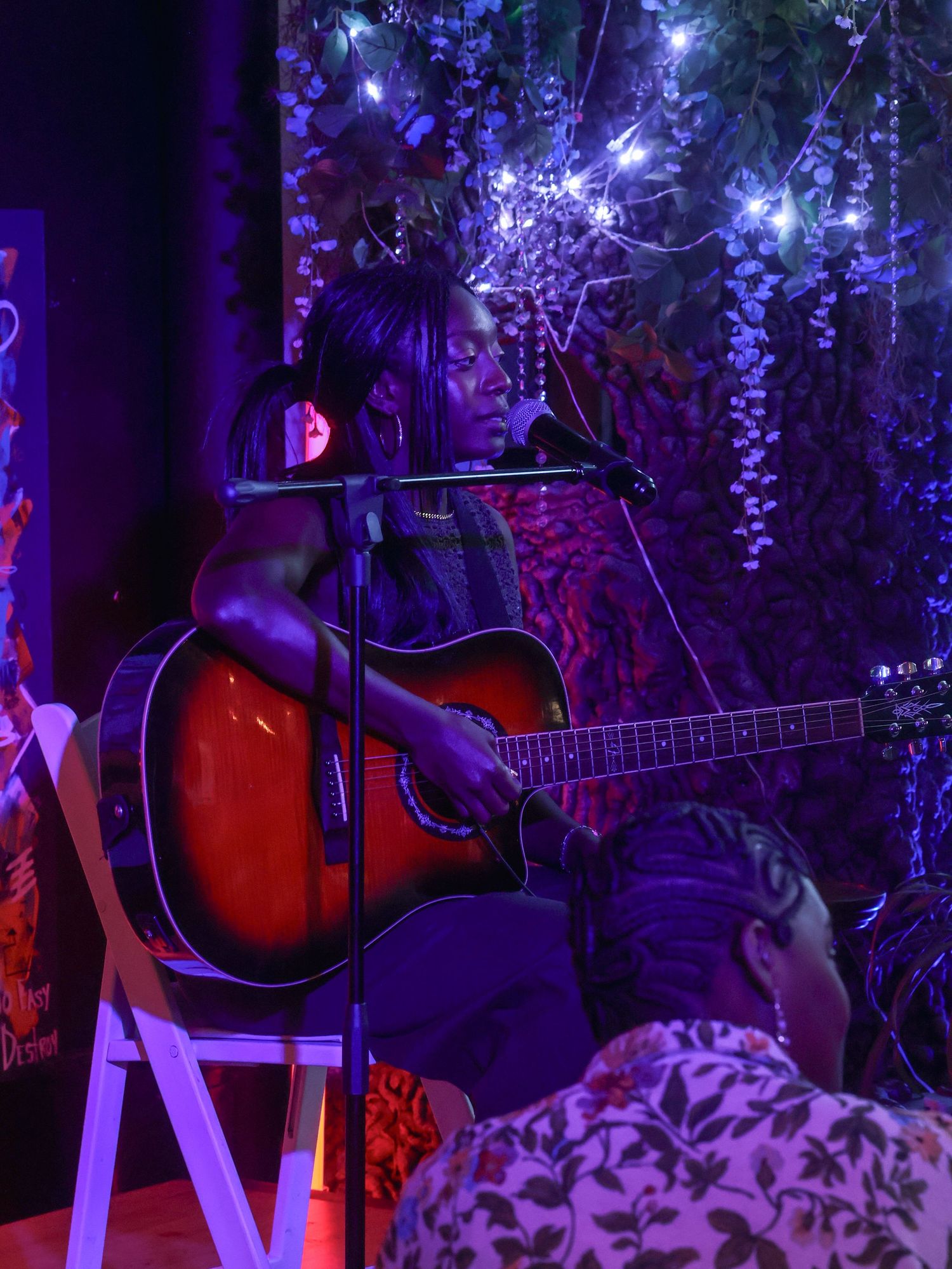 Acoustic guitar sits on stage with purple lighting and hanging floral decorations creating an intimate performance atmosphere.