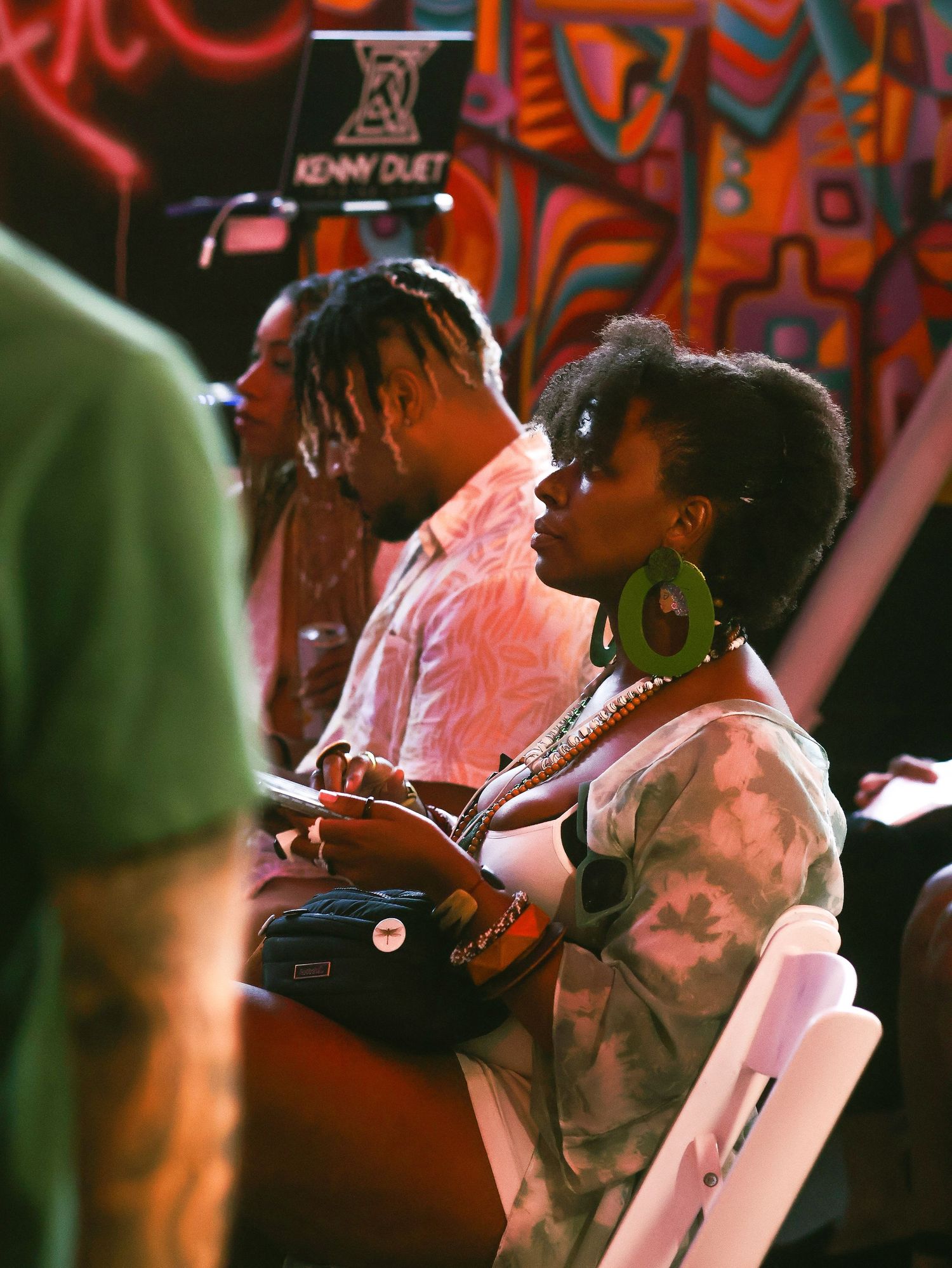 Audience members watch intently in dimly lit venue with red lighting effects.
