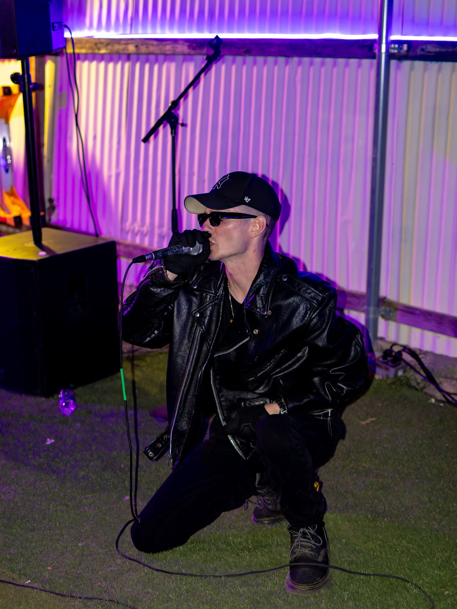 Stage performer in black leather ensemble crouches low during dynamic nightclub performance.