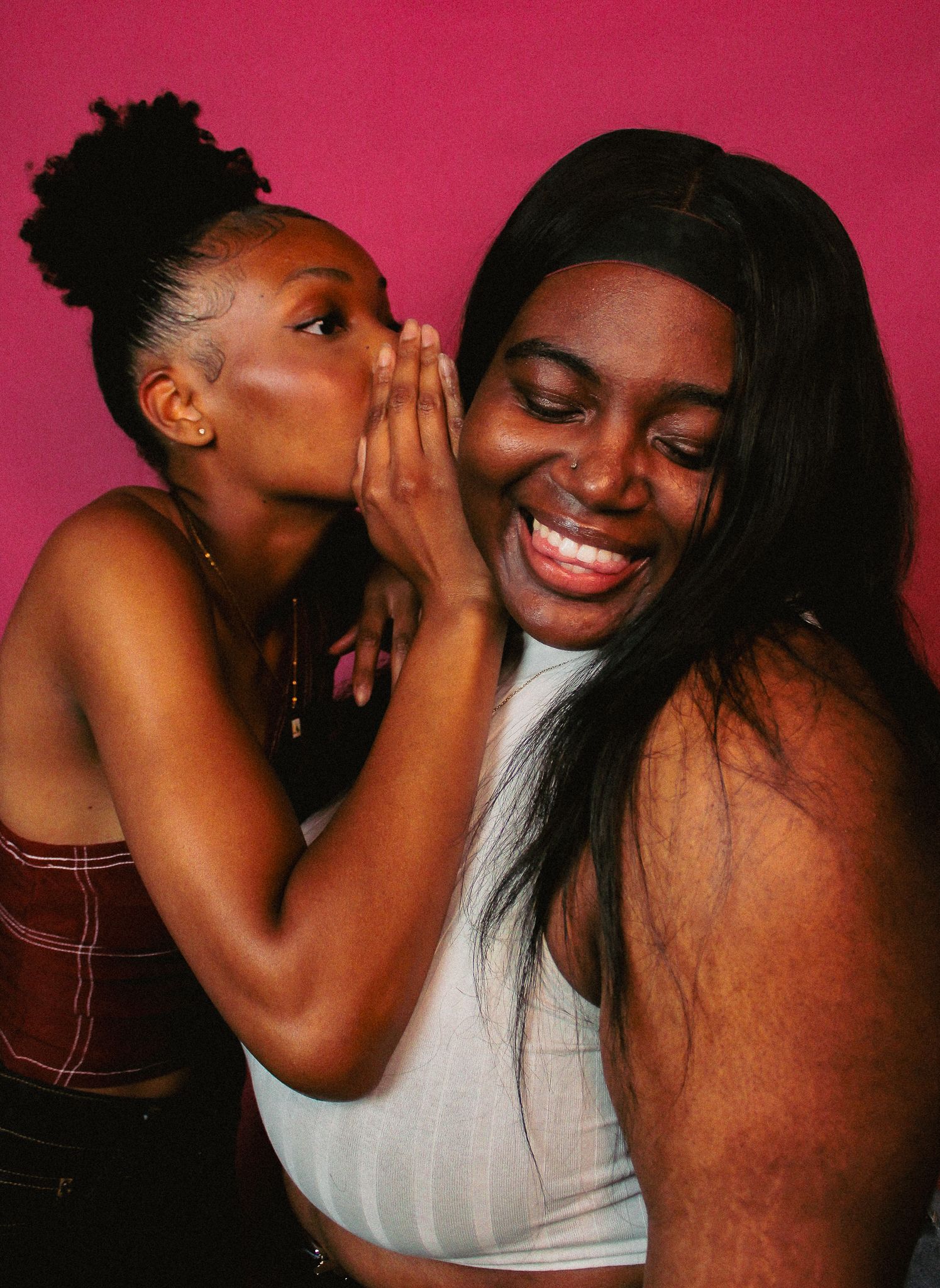 Candid studio portraits show joyful interaction between two people against pink background.