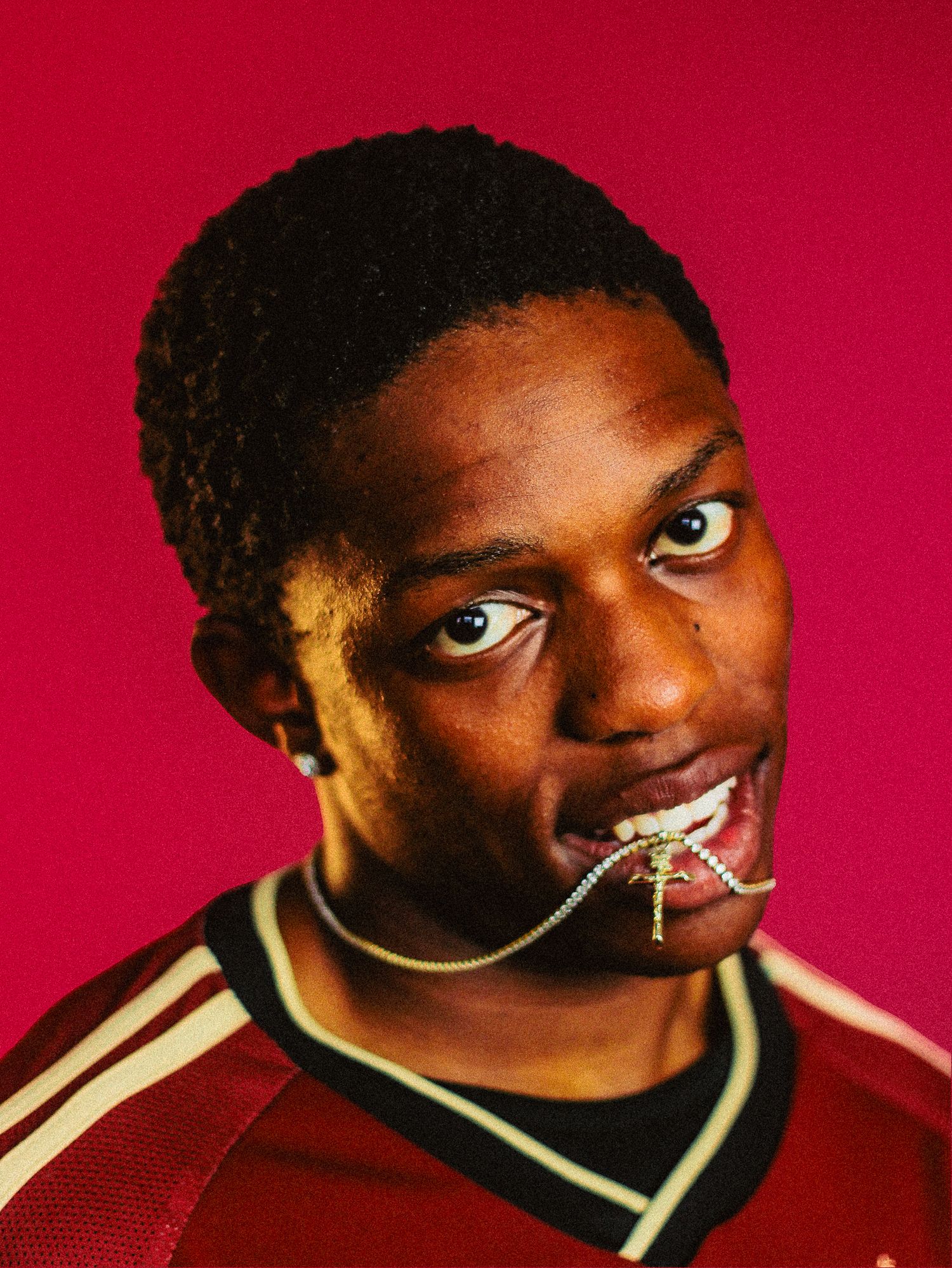 Young man biting a gold chain necklace wearing red jersey on red background.