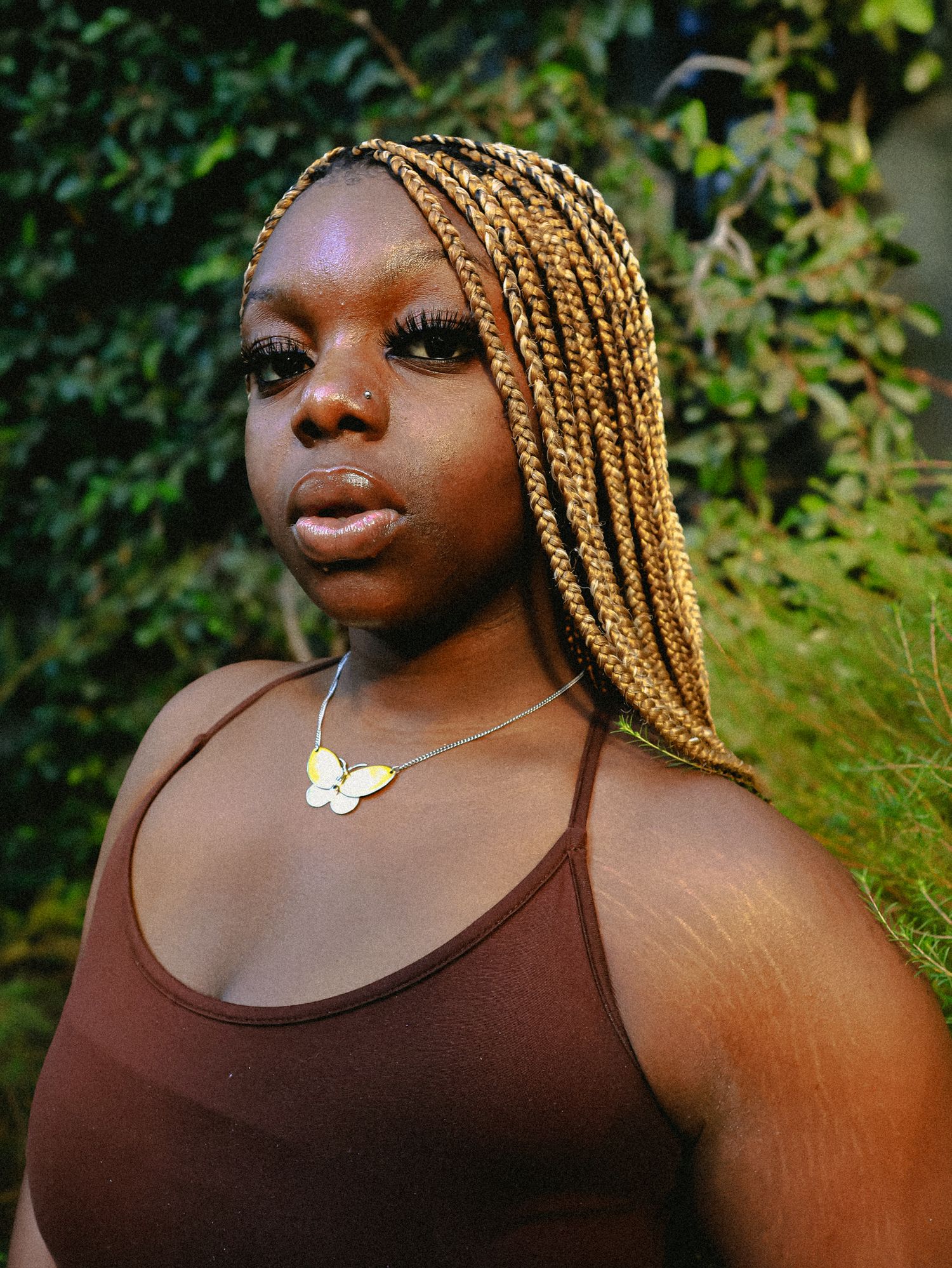 Close-up outdoor portrait with butterfly necklace against garden backdrop.