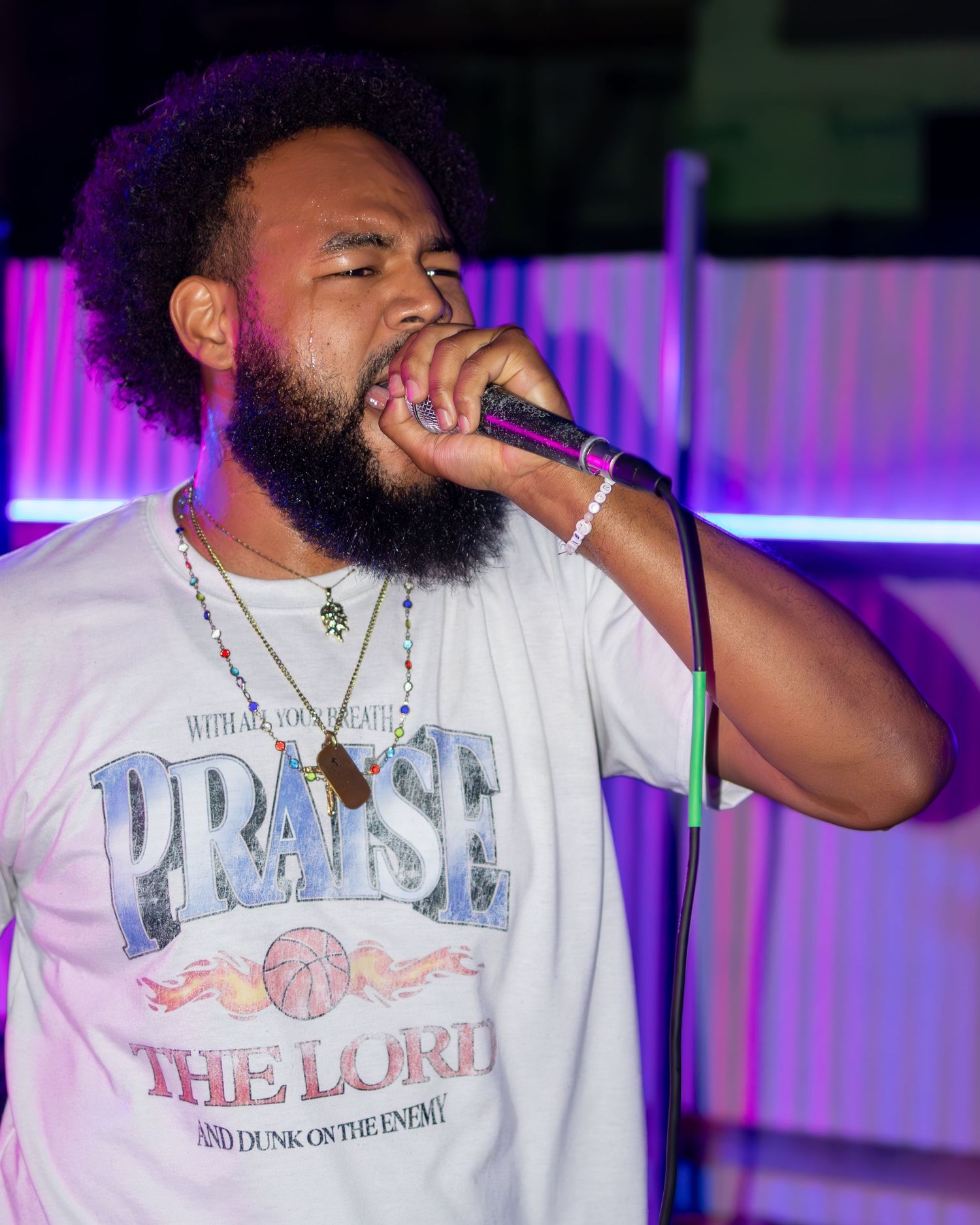 Artist wearing 'Praise' t-shirt performs with microphone under vibrant purple stage lights.