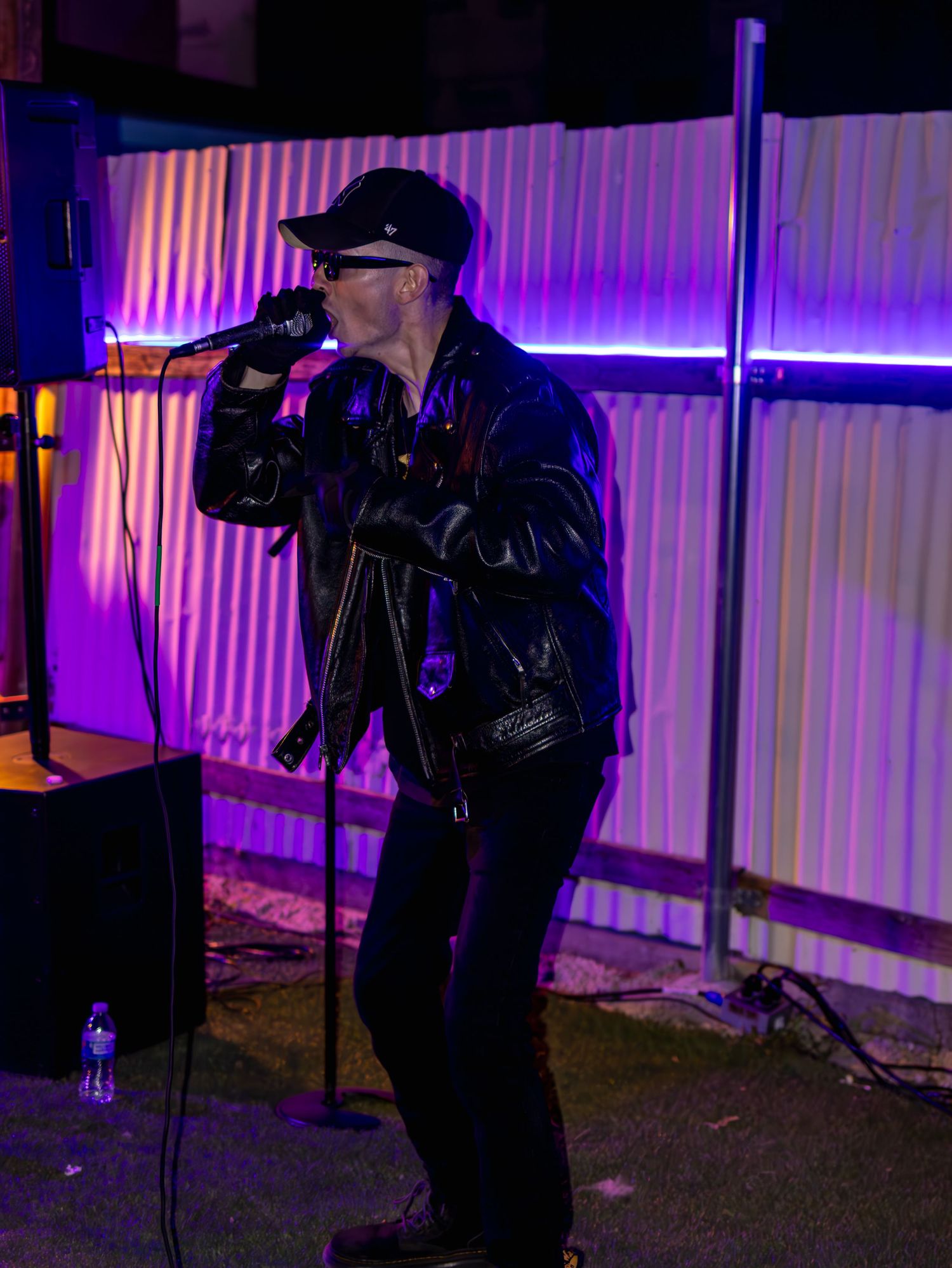 Performer in dark leather jacket and sunglasses singing at night venue.