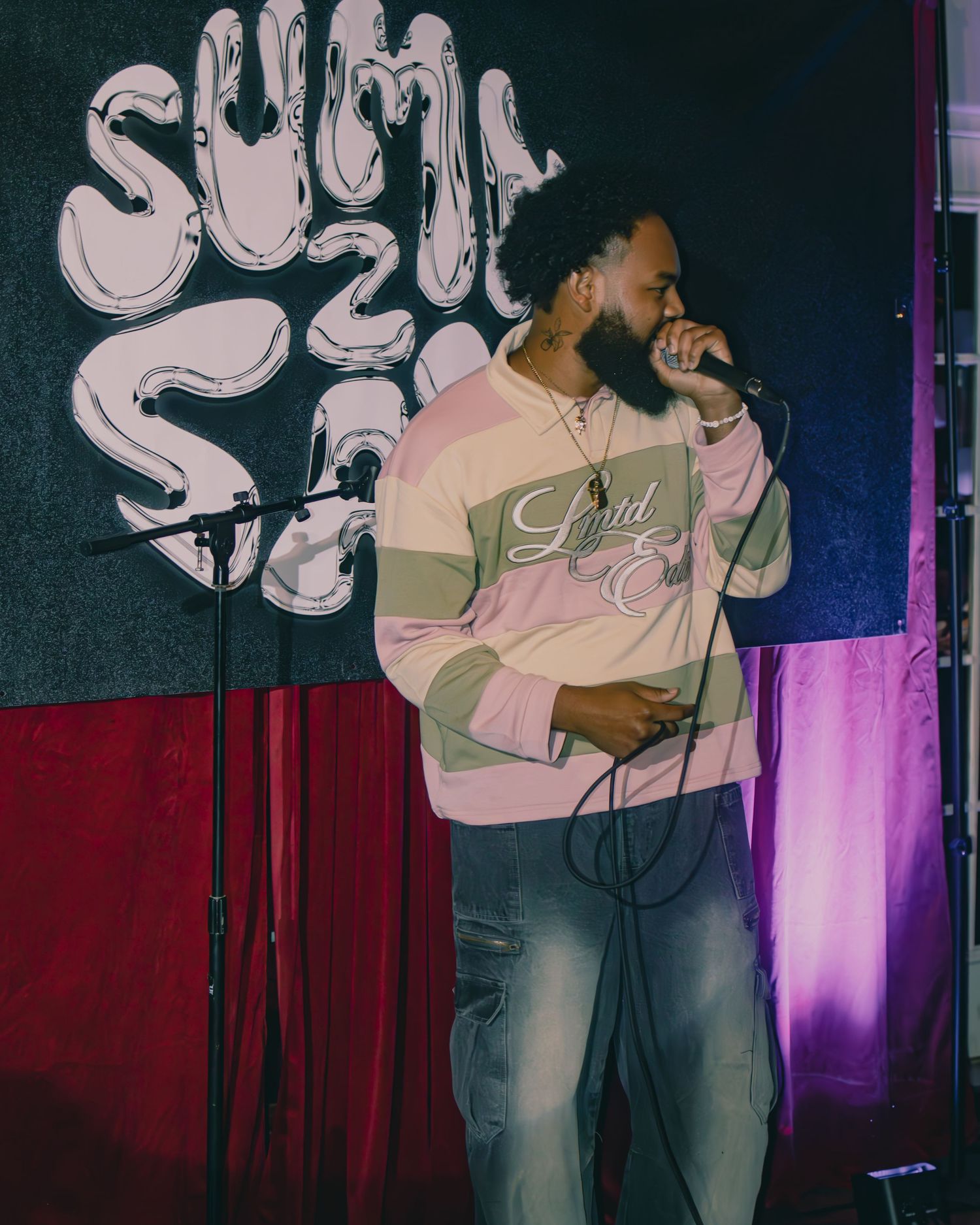 A performer in casual attire singing passionately on stage with purple lighting effects.