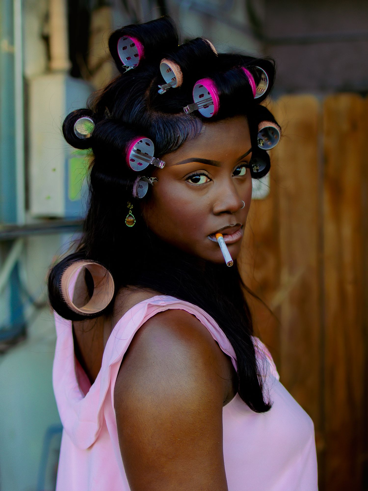 Stylish portrait of model in pink tank top with hair in curlers smoking.