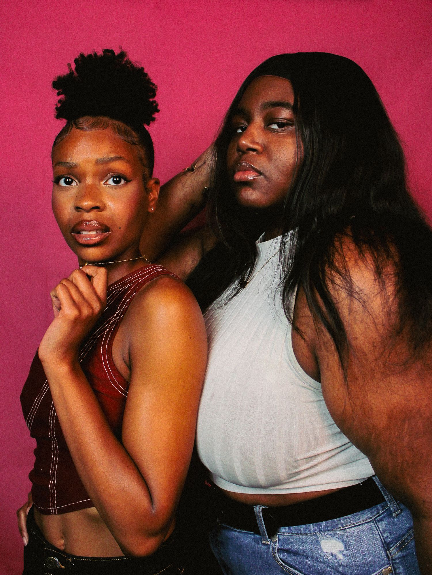 Two people in casual attire strike dynamic poses during a photo shoot with pink background.