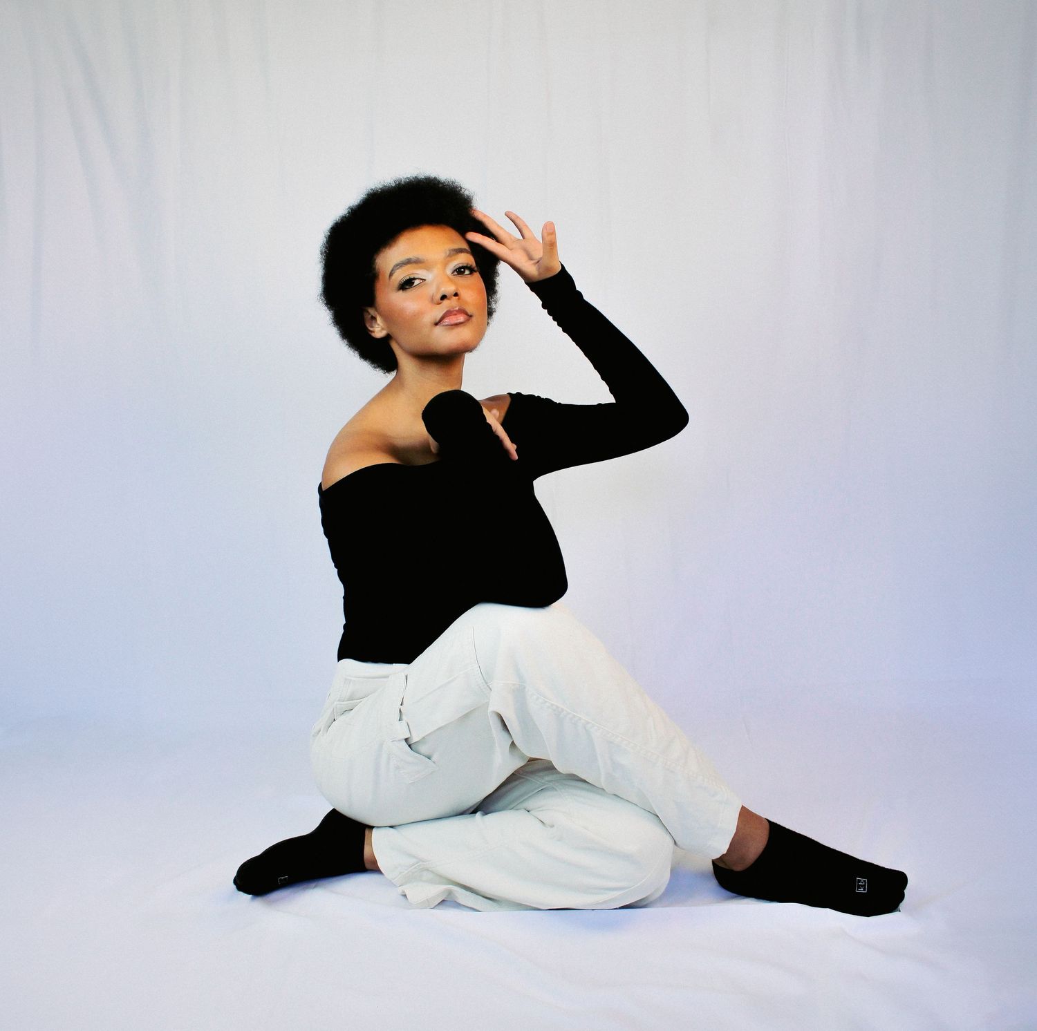 Person in black top and white pants performing expressive dance poses on white background.