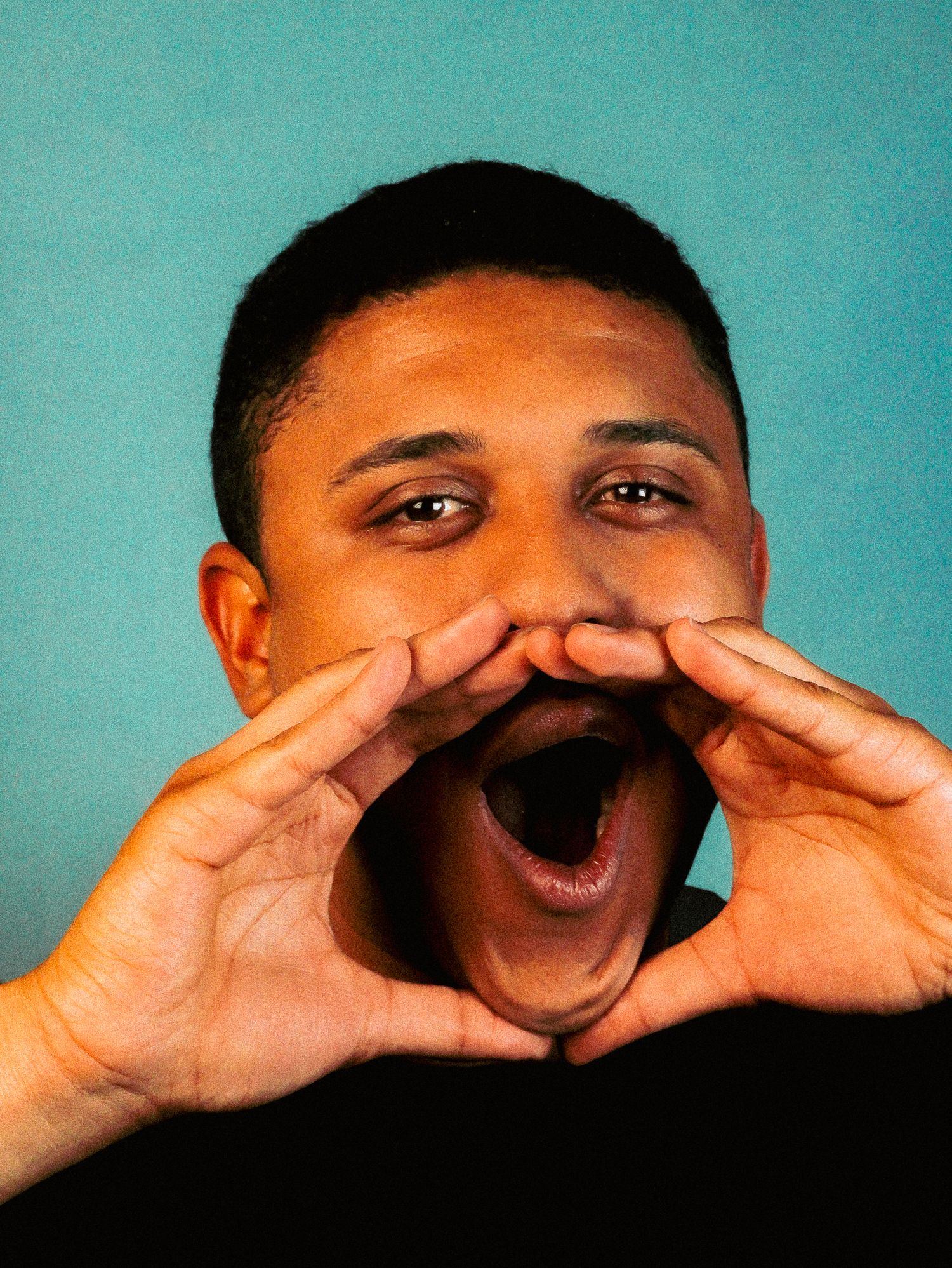 Young man cupping hands around mouth as if shouting against a teal background.