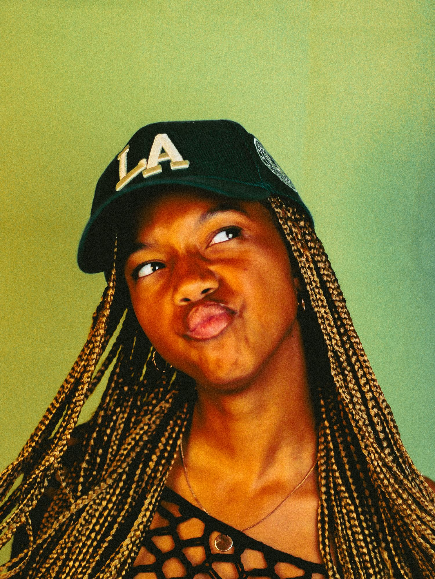 Young Black woman with long box braids making a pouty expression wearing a navy LA baseball cap.