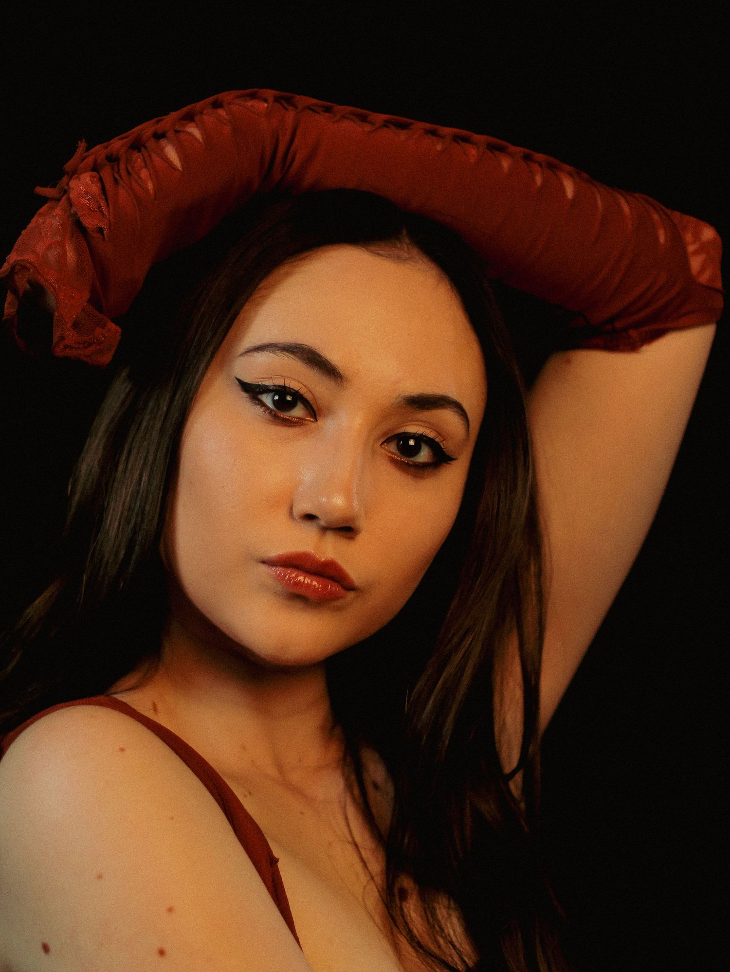 Portrait in warm lighting with dramatic red tones and dark background.