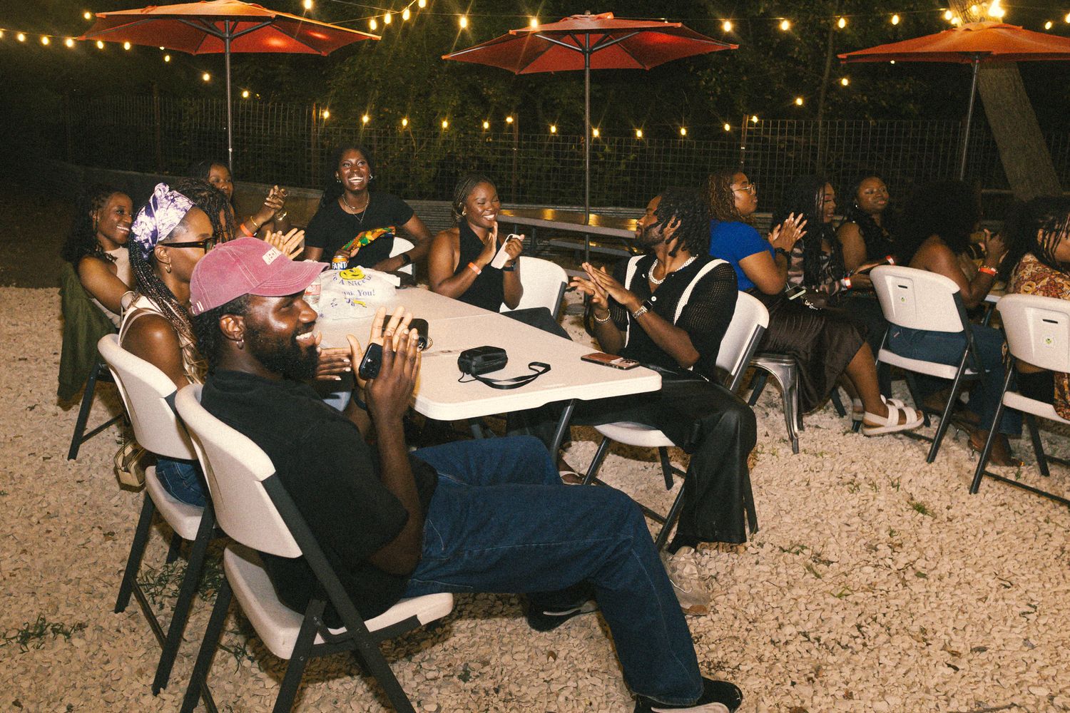 String lights illuminate an outdoor patio seating area at night with tables and umbrellas.