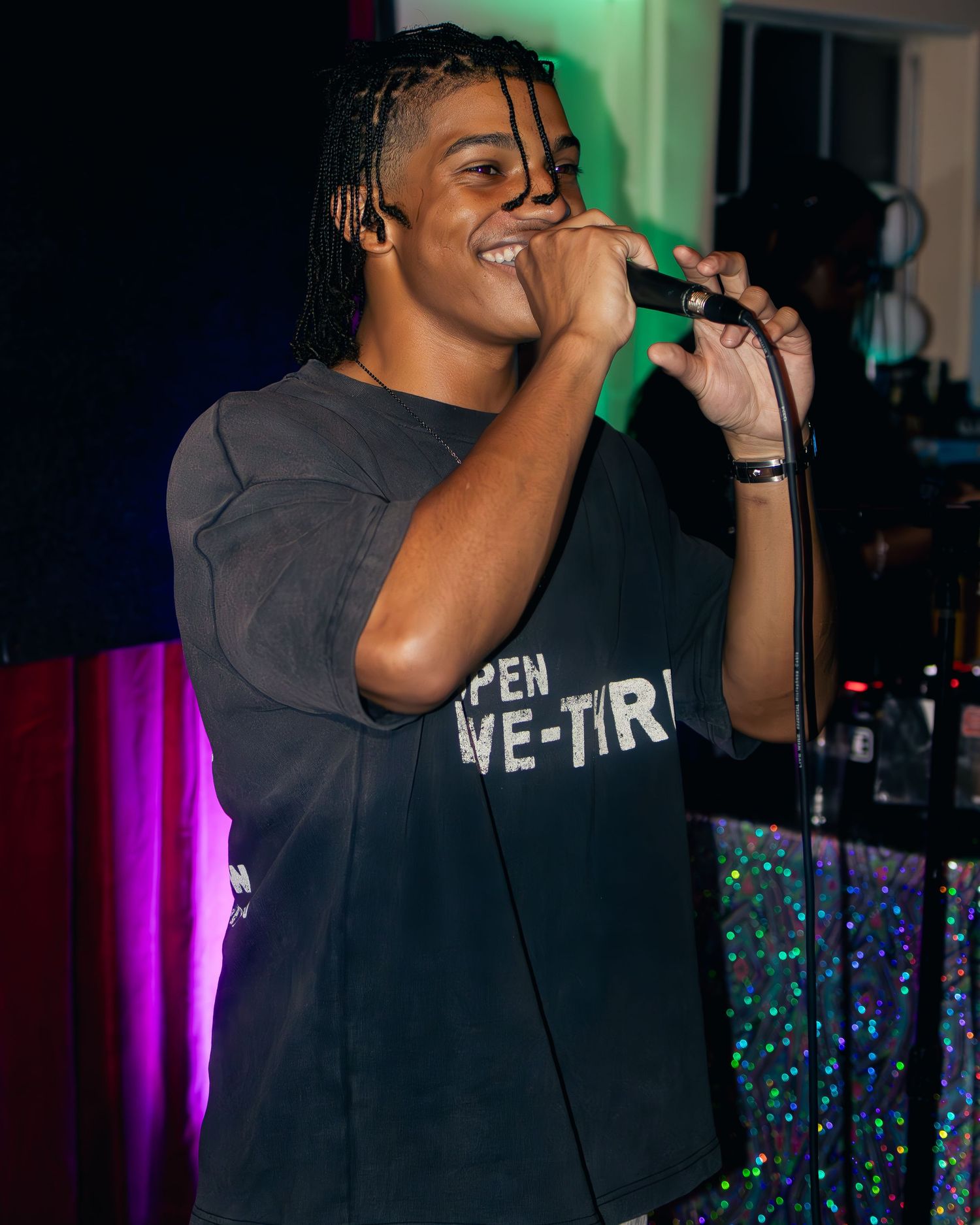 Singer wearing dark t-shirt performing under green stage lighting at indoor venue.