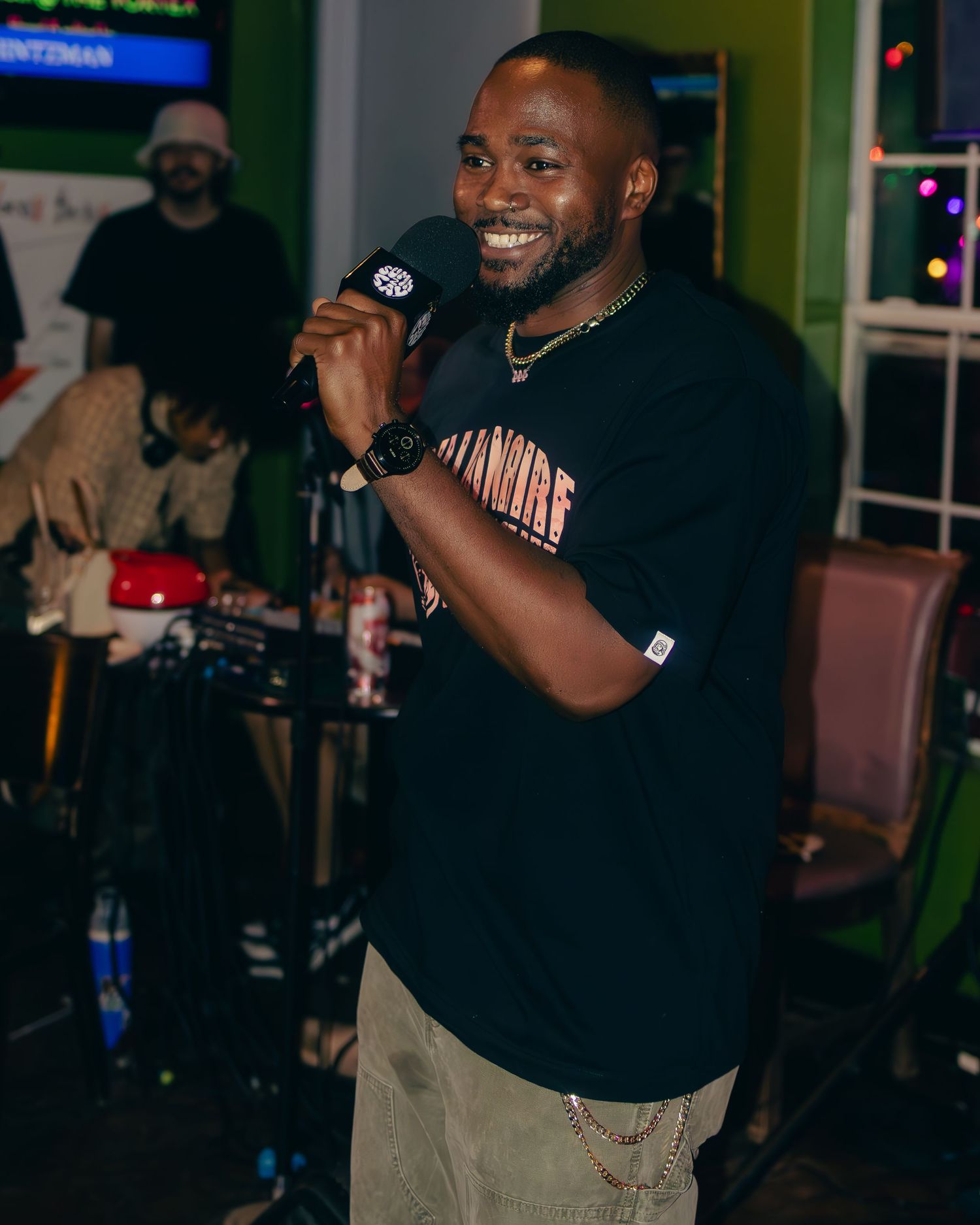 Enthusiastic performer smiling while speaking into microphone at nightclub event.