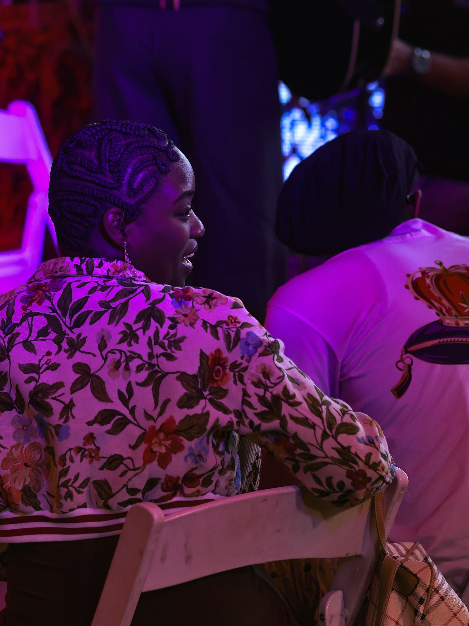 Row of people seated in chairs with floral patterns visible under purple lighting.