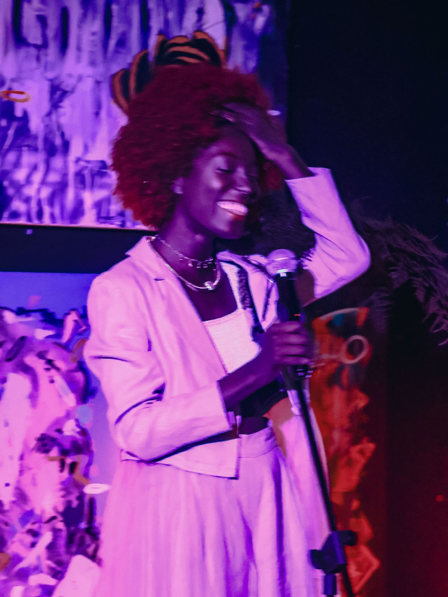 A musical performance featuring a singer in white under colorful stage lighting.
