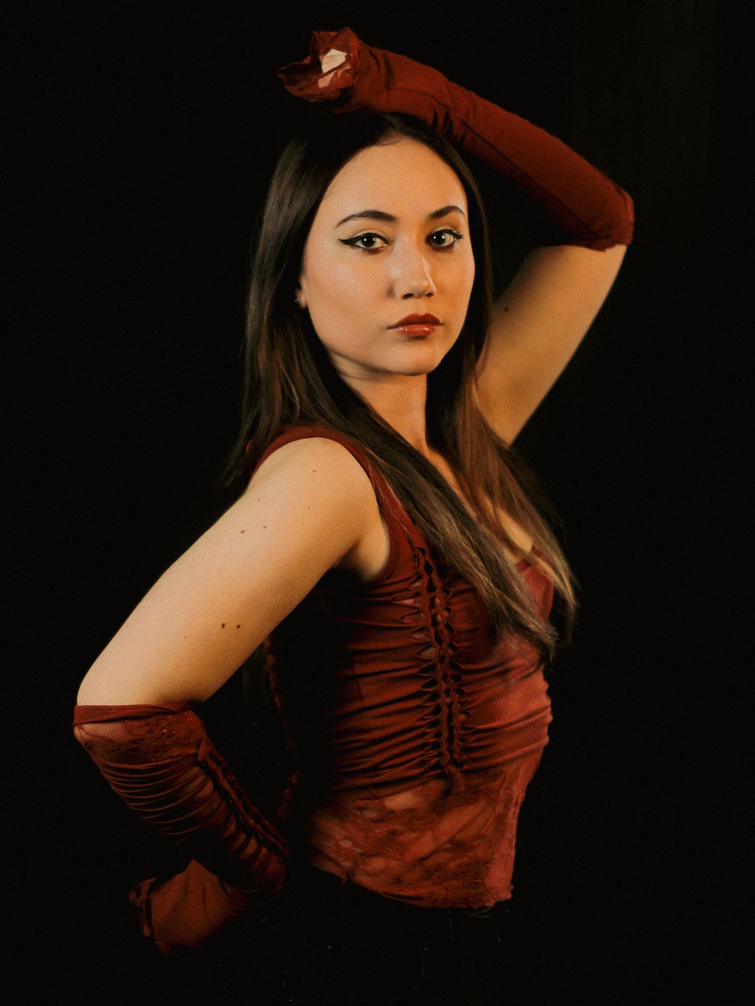 Dramatic studio portrait in burgundy dress against black background.