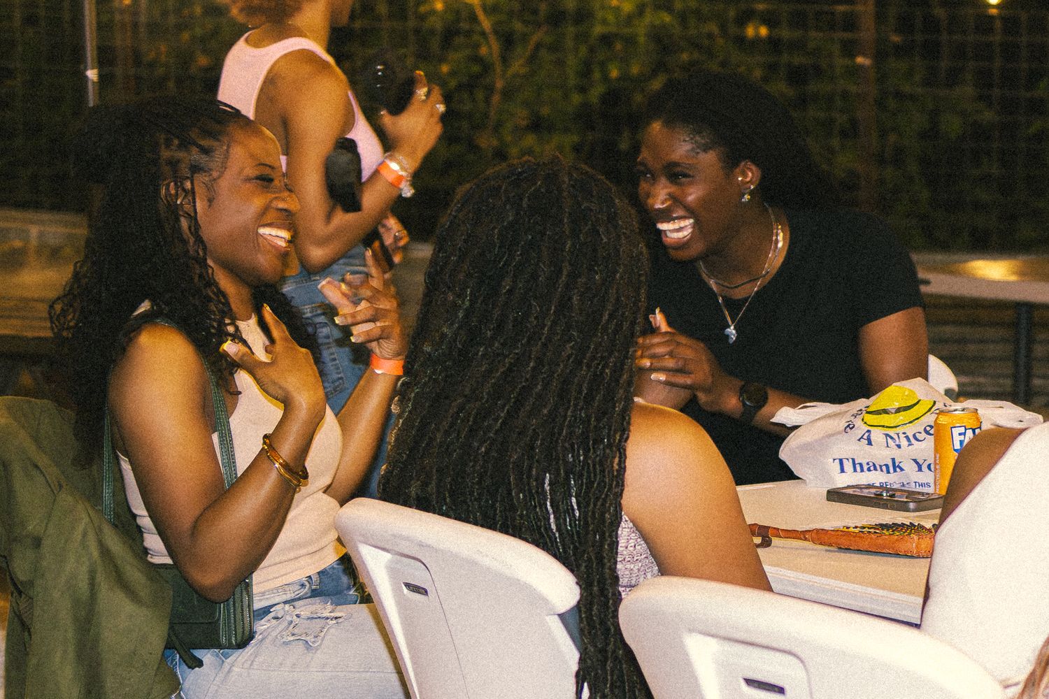 Friends gathered around tables laughing and socializing at an outdoor evening event.