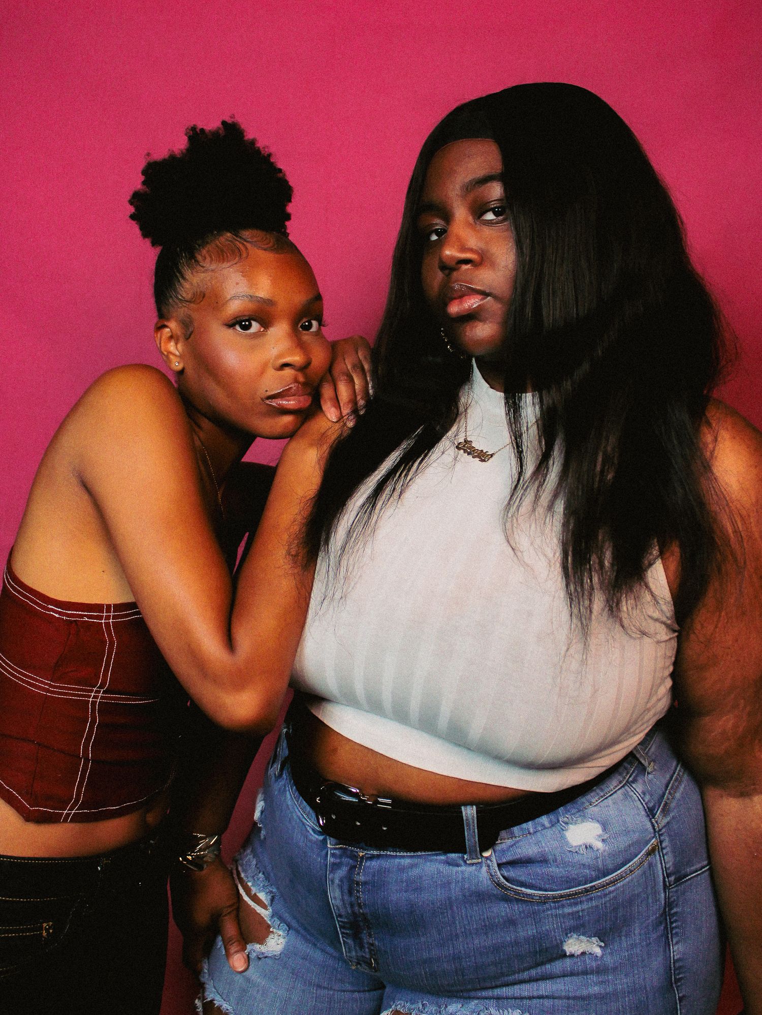 Two people embrace casually while posing against a vibrant pink background.