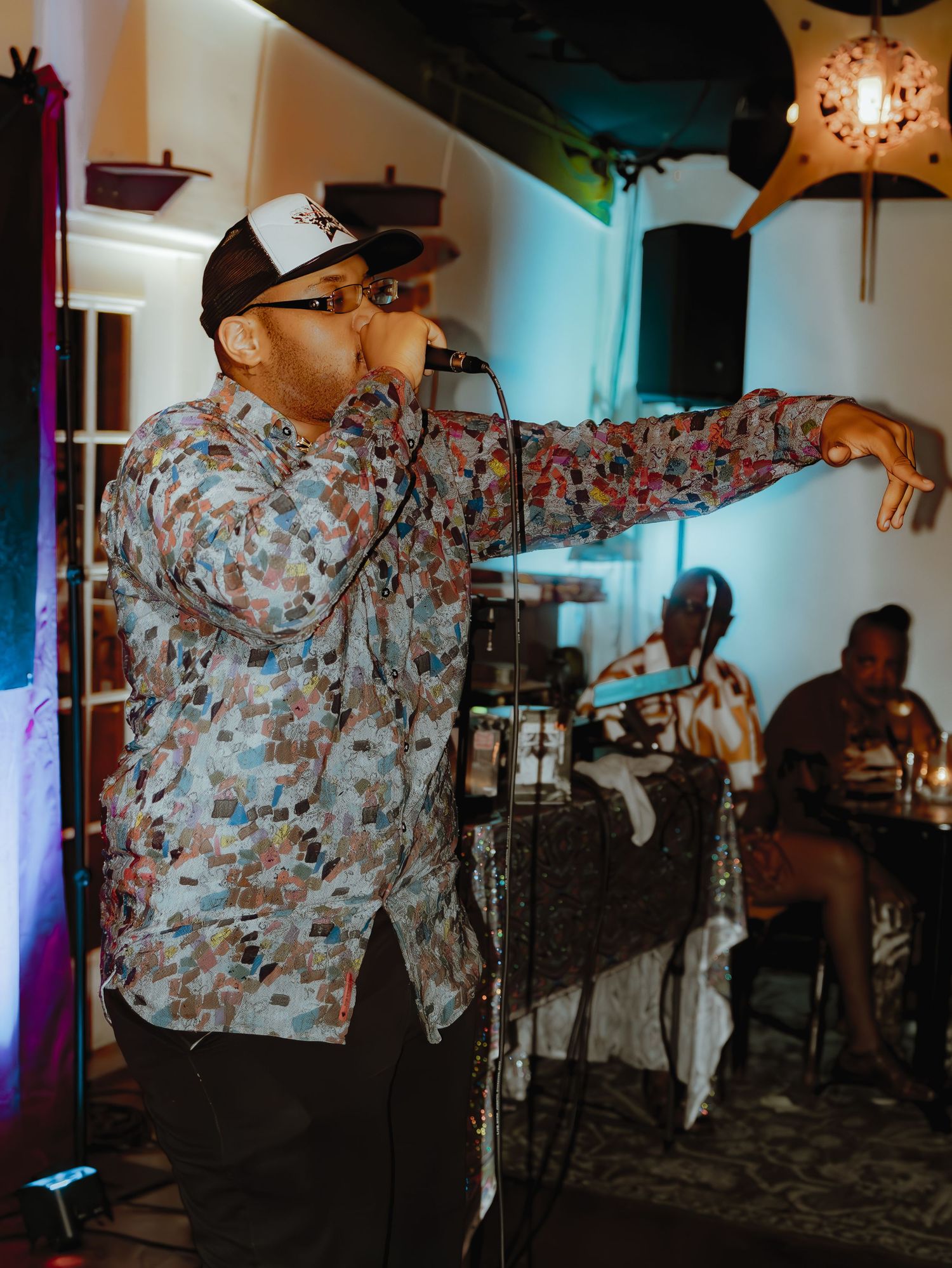 A performer in a patterned shirt delivers an animated performance under colorful stage lights.