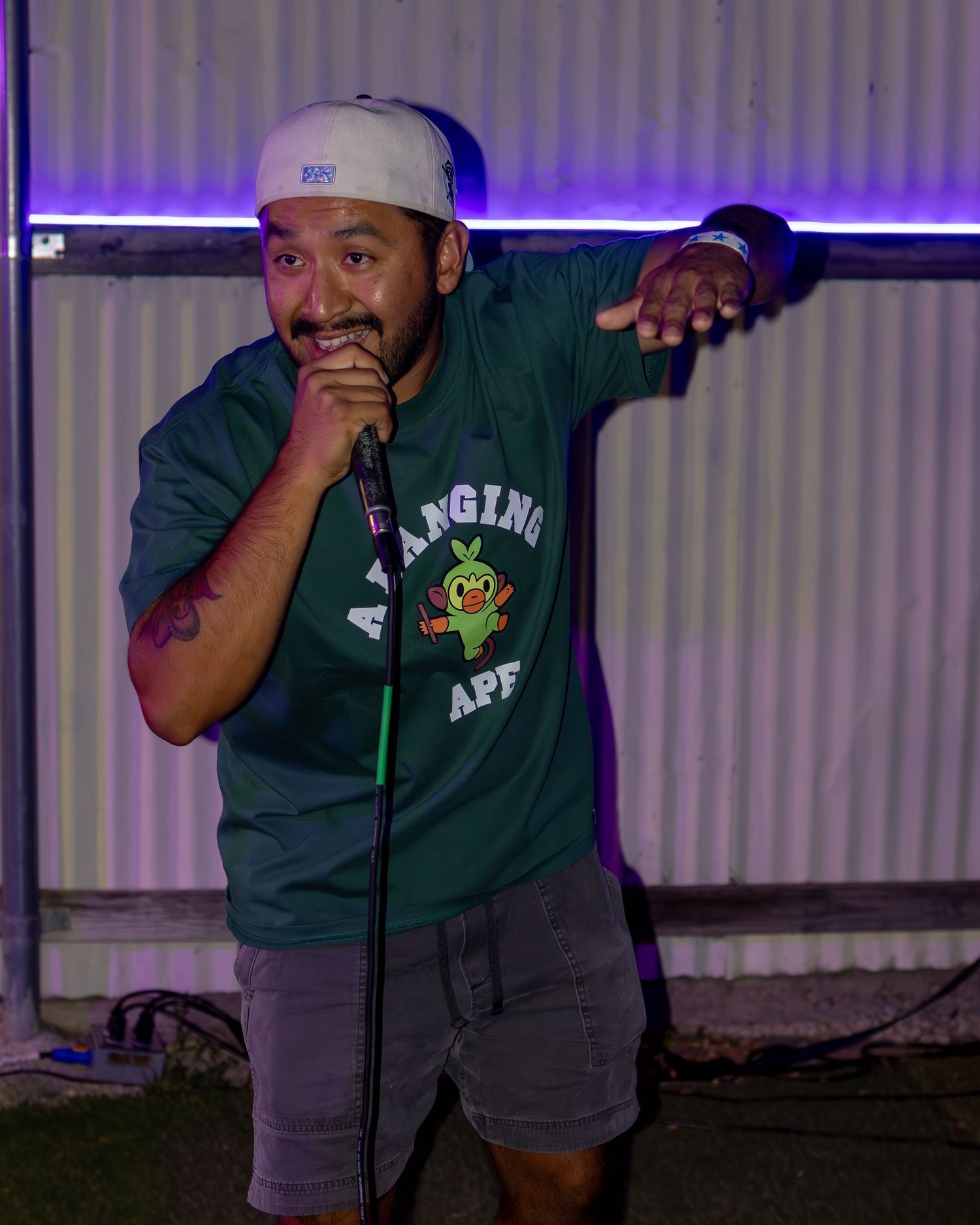 Performer in green shirt gesturing animatedly while using microphone on stage.
