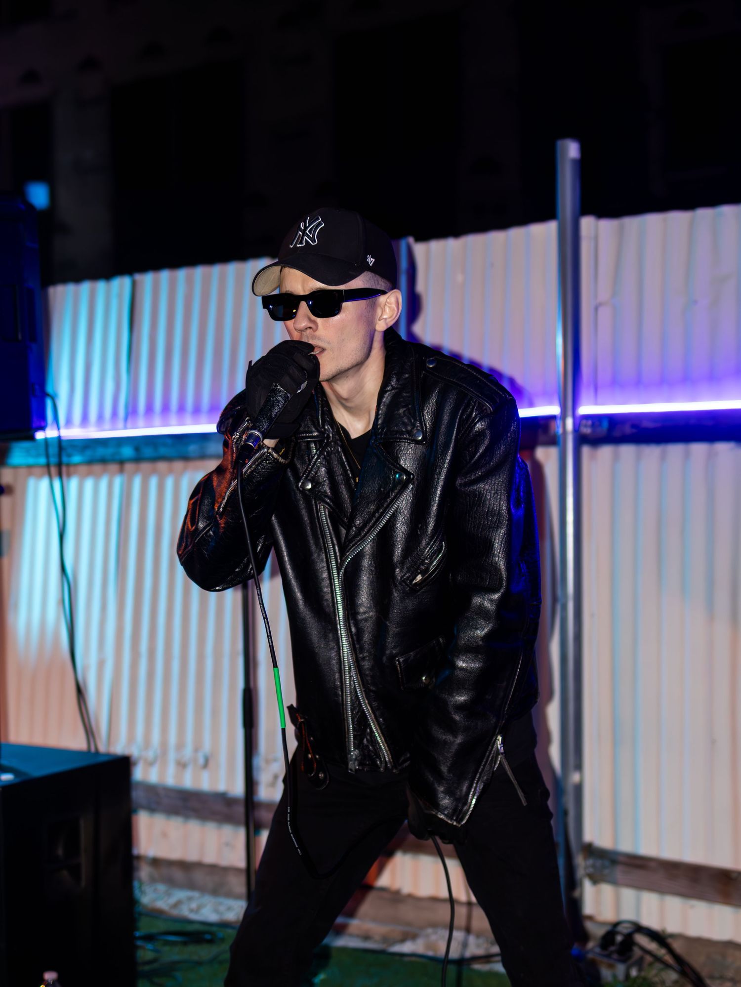 Performer in all black outfit strikes dramatic pose during nighttime show.