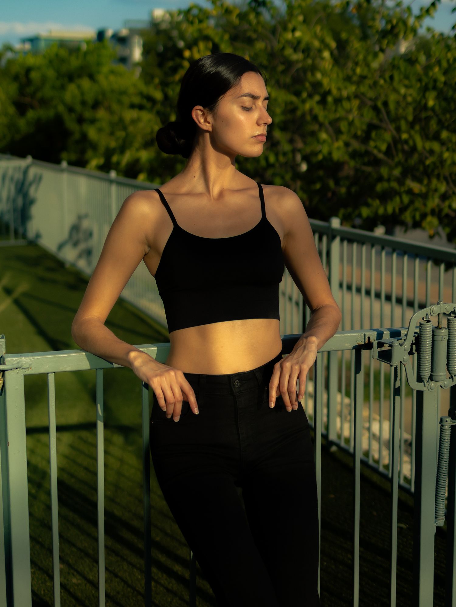 Athletic figure leans against white railing during golden hour photoshoot.