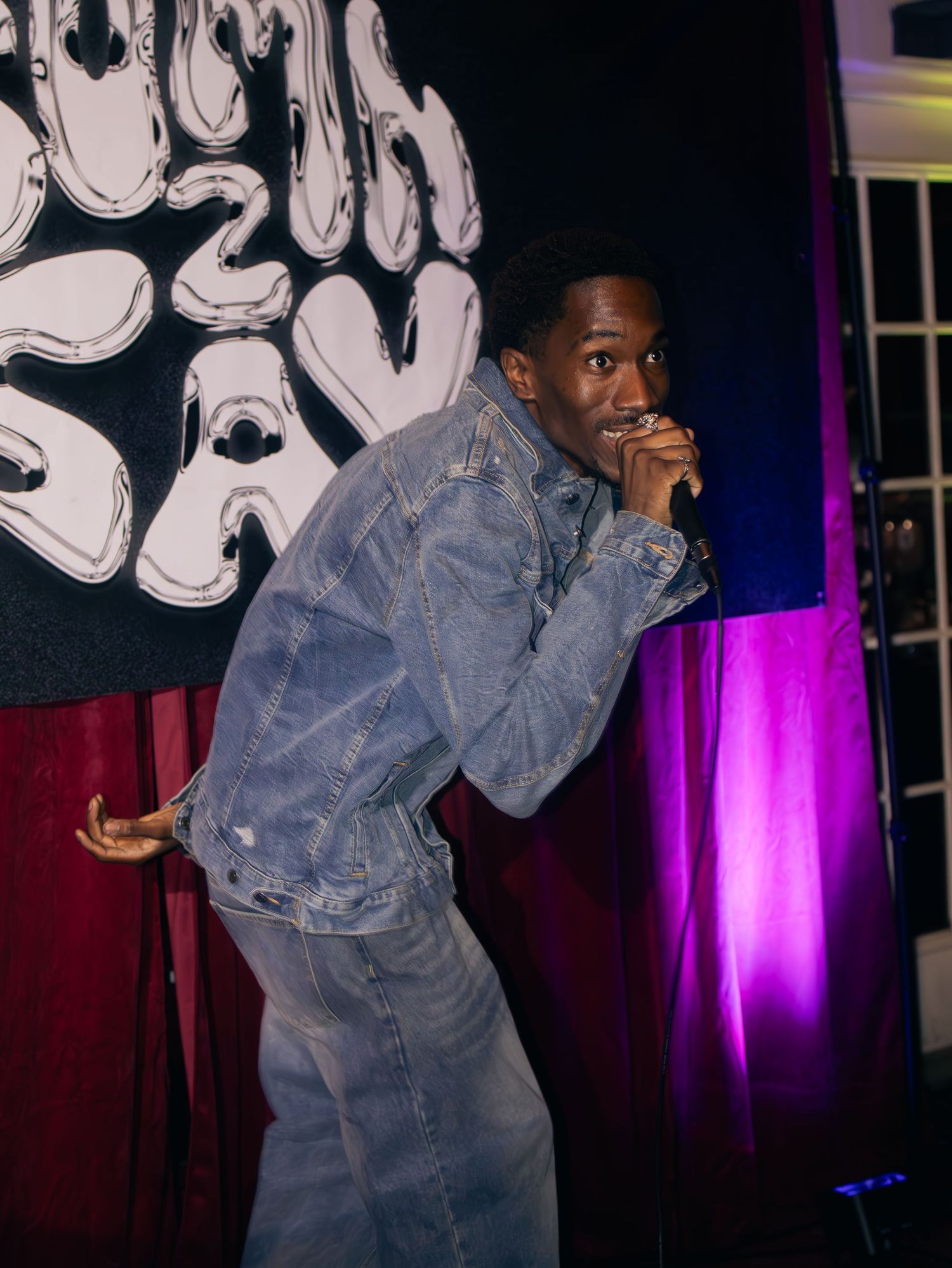 Artist in denim outfit performing with animated gestures against dramatic purple stage lighting.