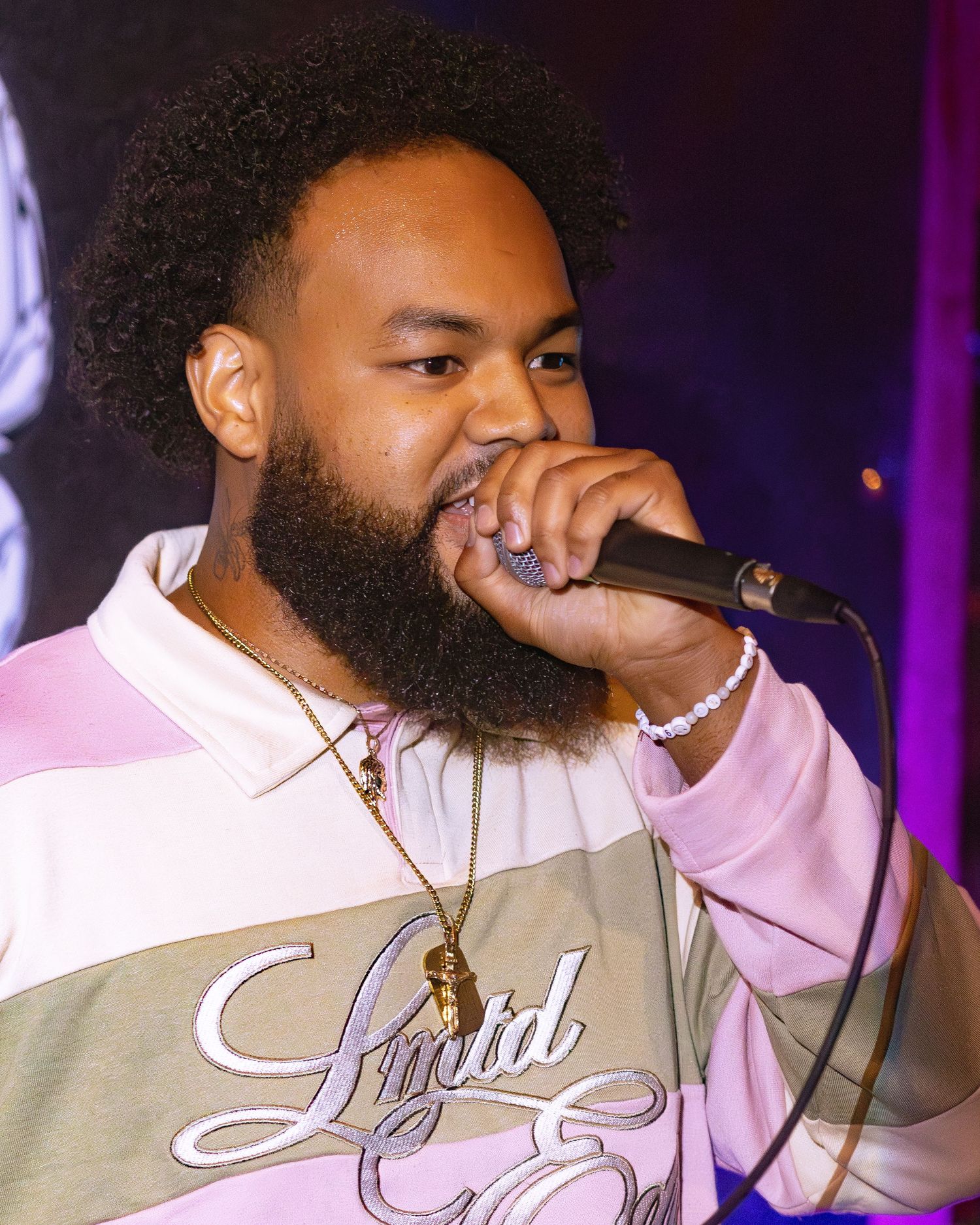 Performer in a pink and gray striped shirt singing passionately into a microphone.