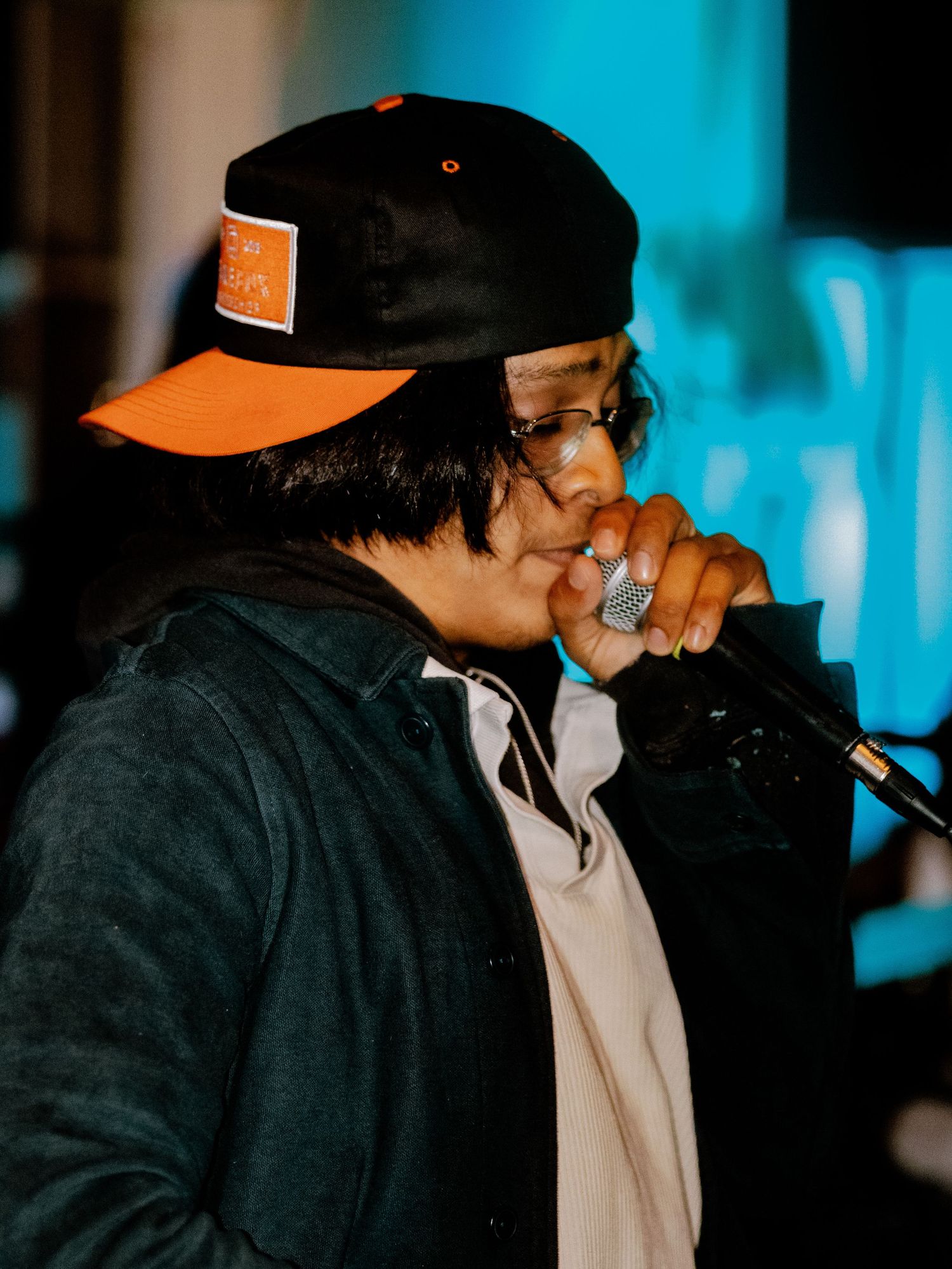 Performer in black cap and white shirt on stage with blue lighting.