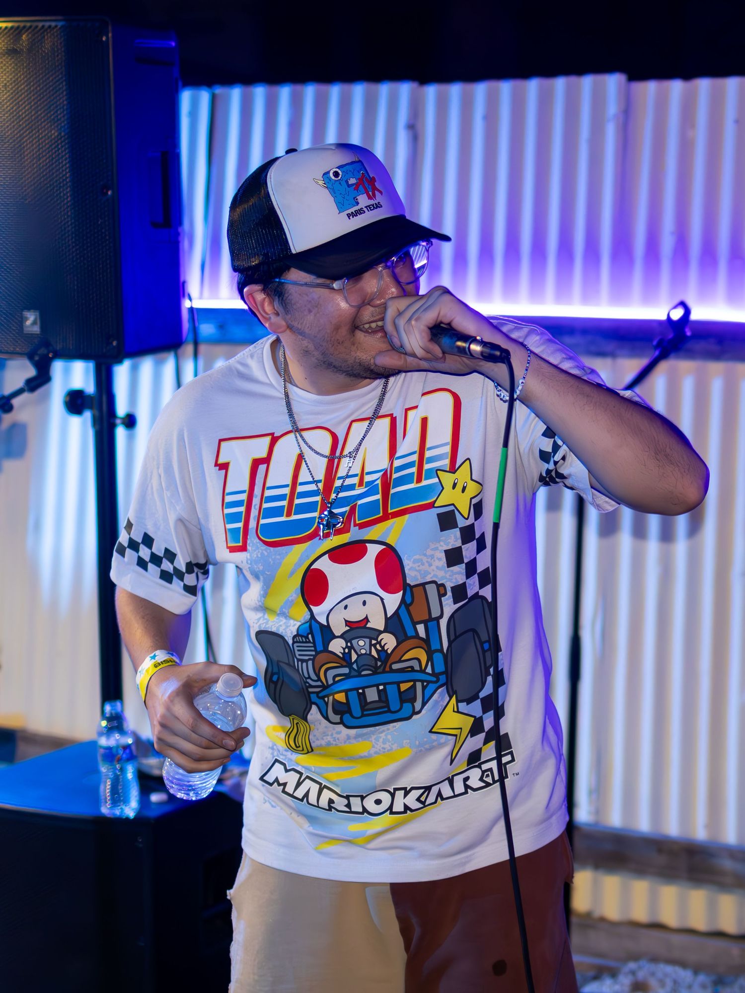 Performer wearing Mario Kart themed t-shirt singing on illuminated stage.
