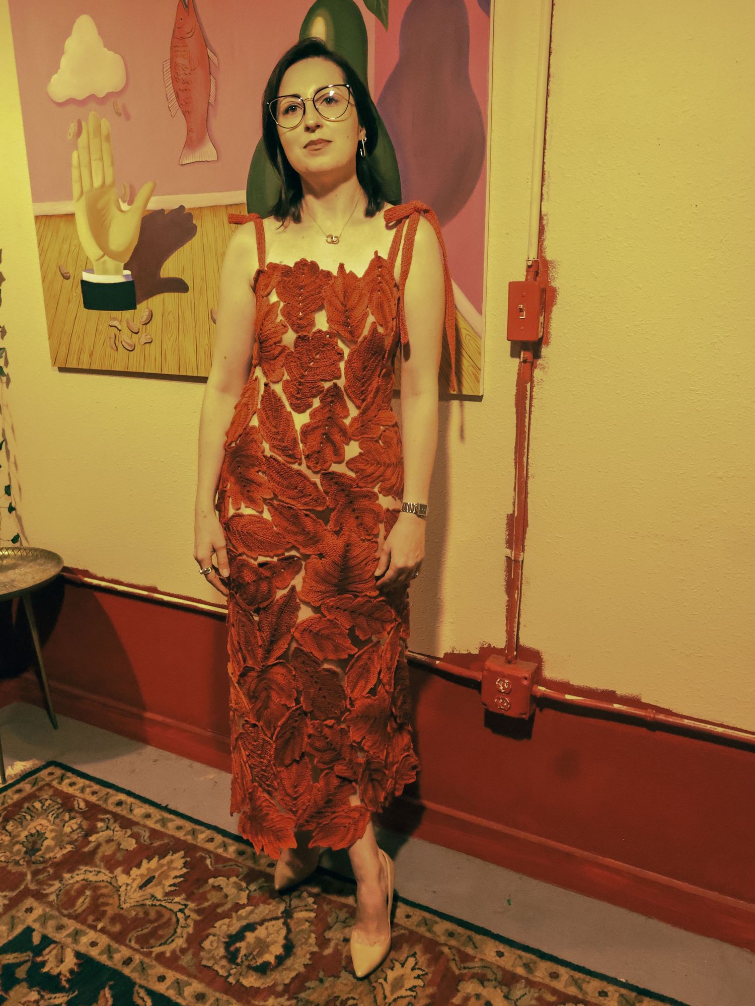 A red lace dress is shown in a room with beige walls and decorative artwork.