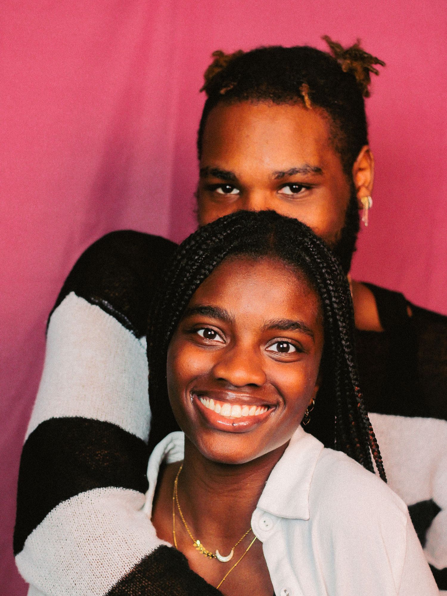 Close-up portrait against pink background showing bright smile and braided hairstyle.