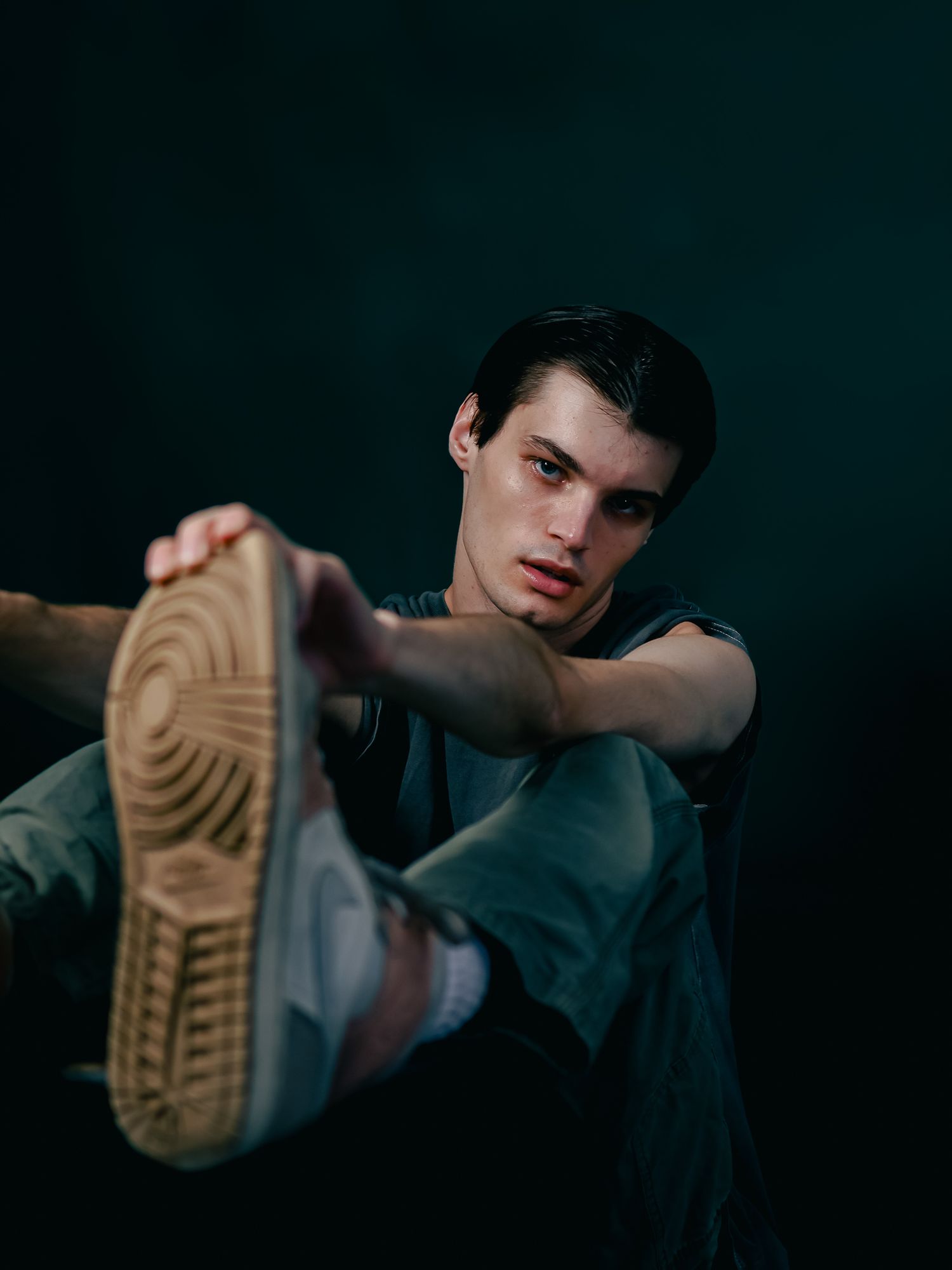 Moody portrait of person in casual wear stretching leg against dark background.
