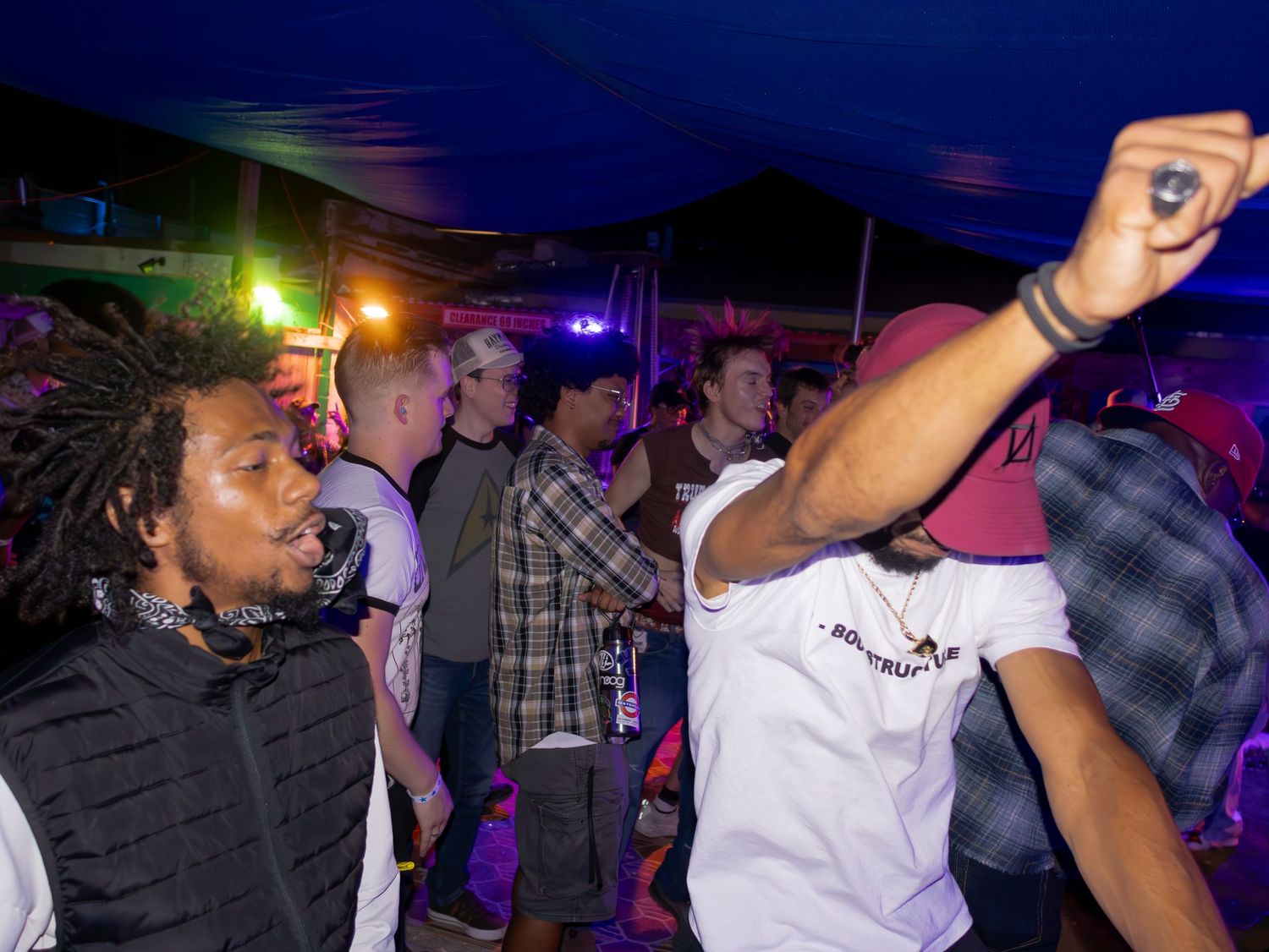 Energetic crowd dancing at a music event with vibrant lighting and dark atmosphere.