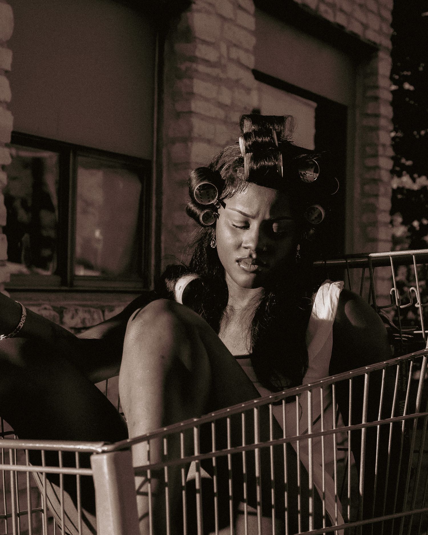 Monochrome portrait of model resting in shopping cart with curlers in hair.