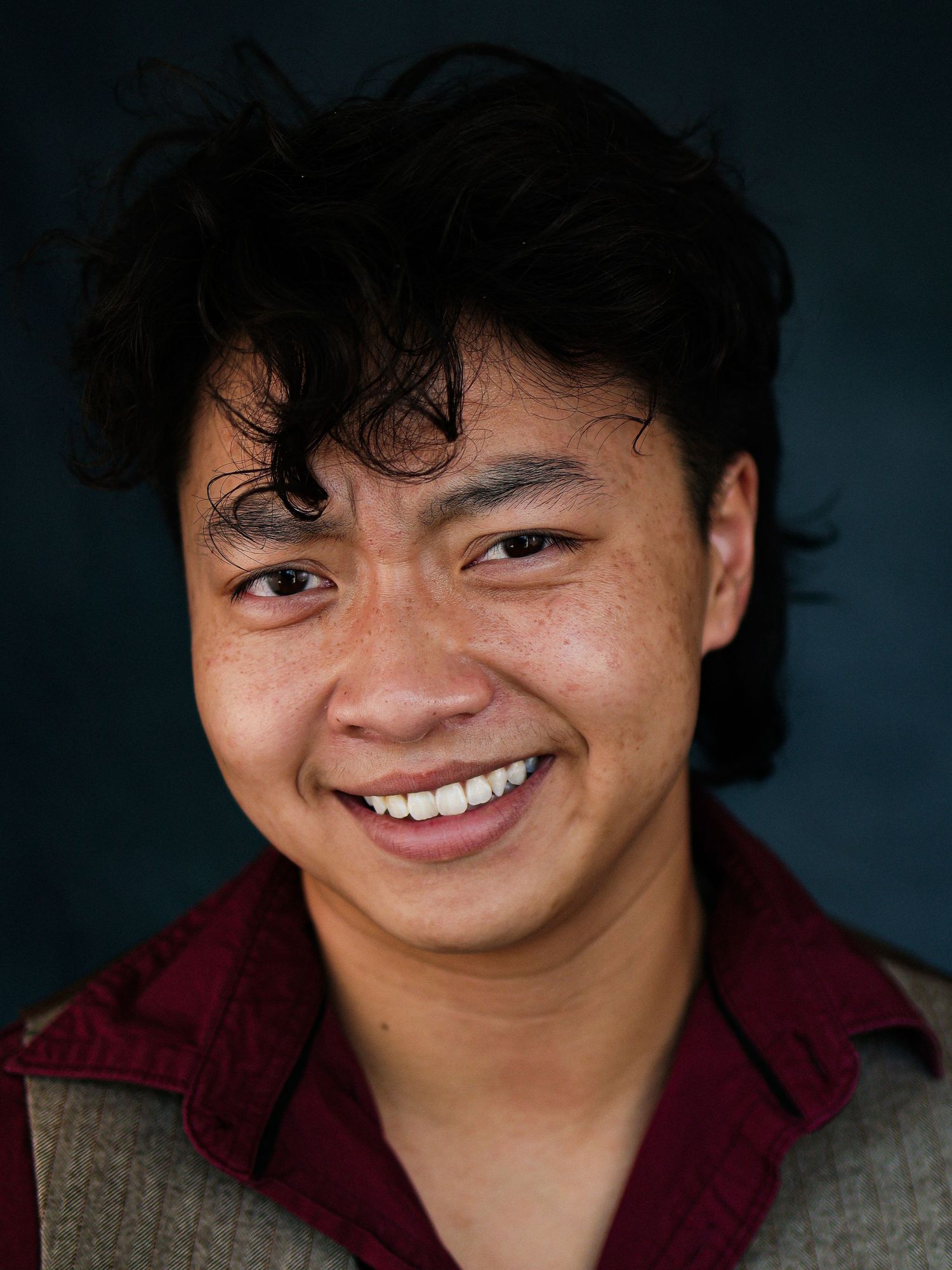 Studio portrait in burgundy shirt showing warm smile against dark background.