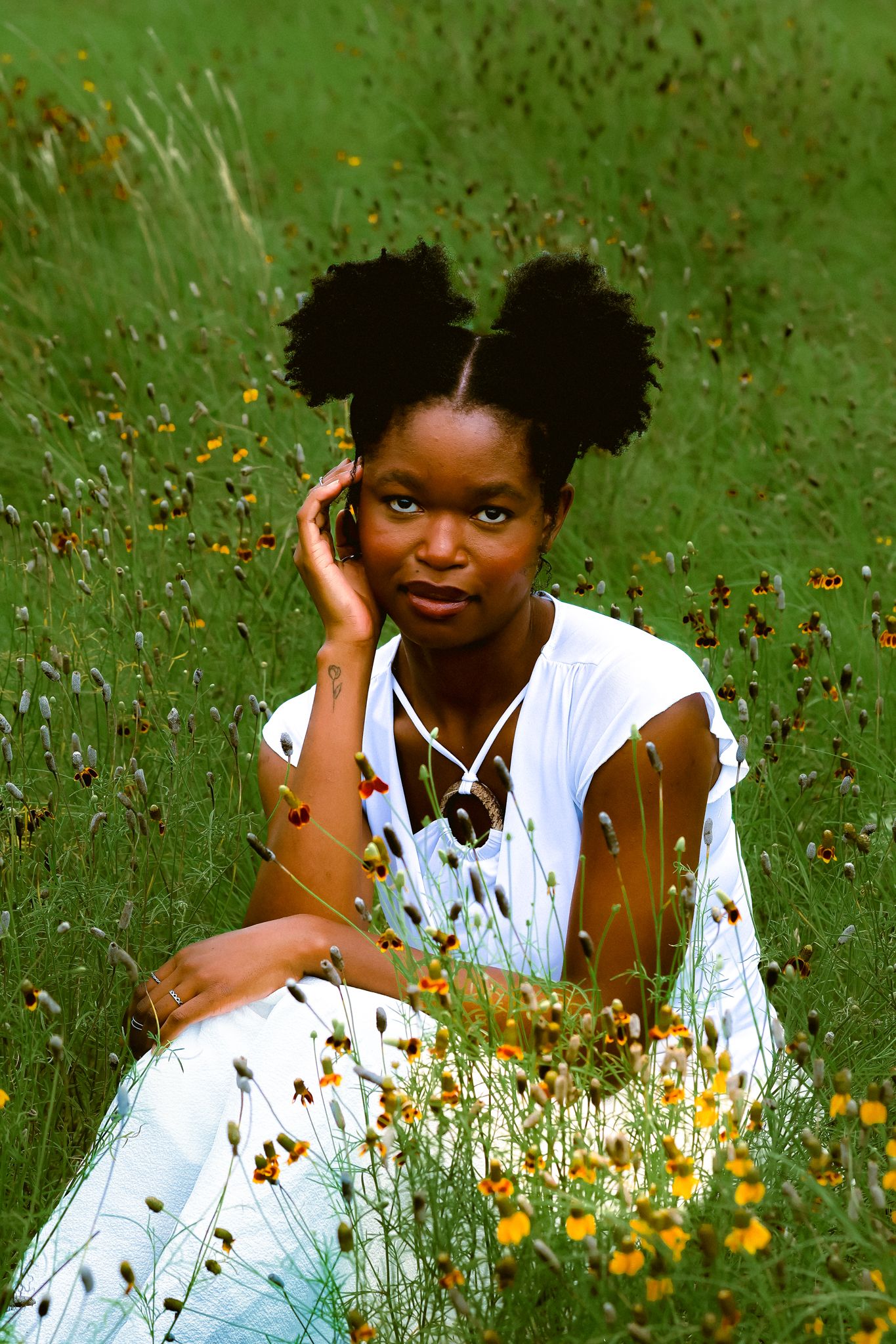 A person in a white dress lies in a field of wildflowers on a sunny day.