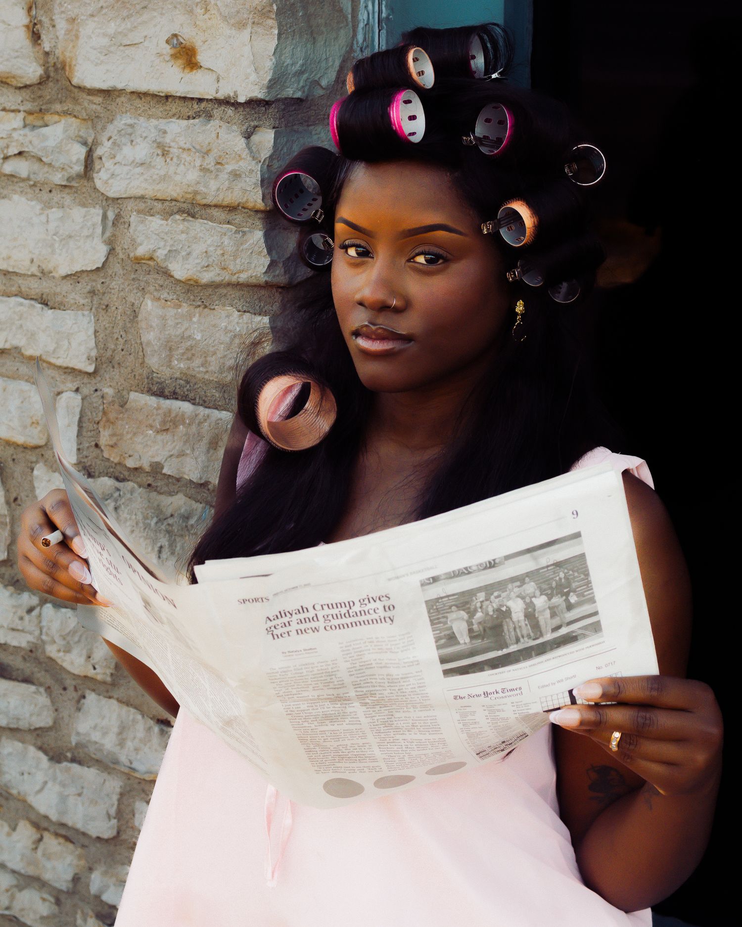 A person with curlers in their hair holds up and reads from a newspaper.