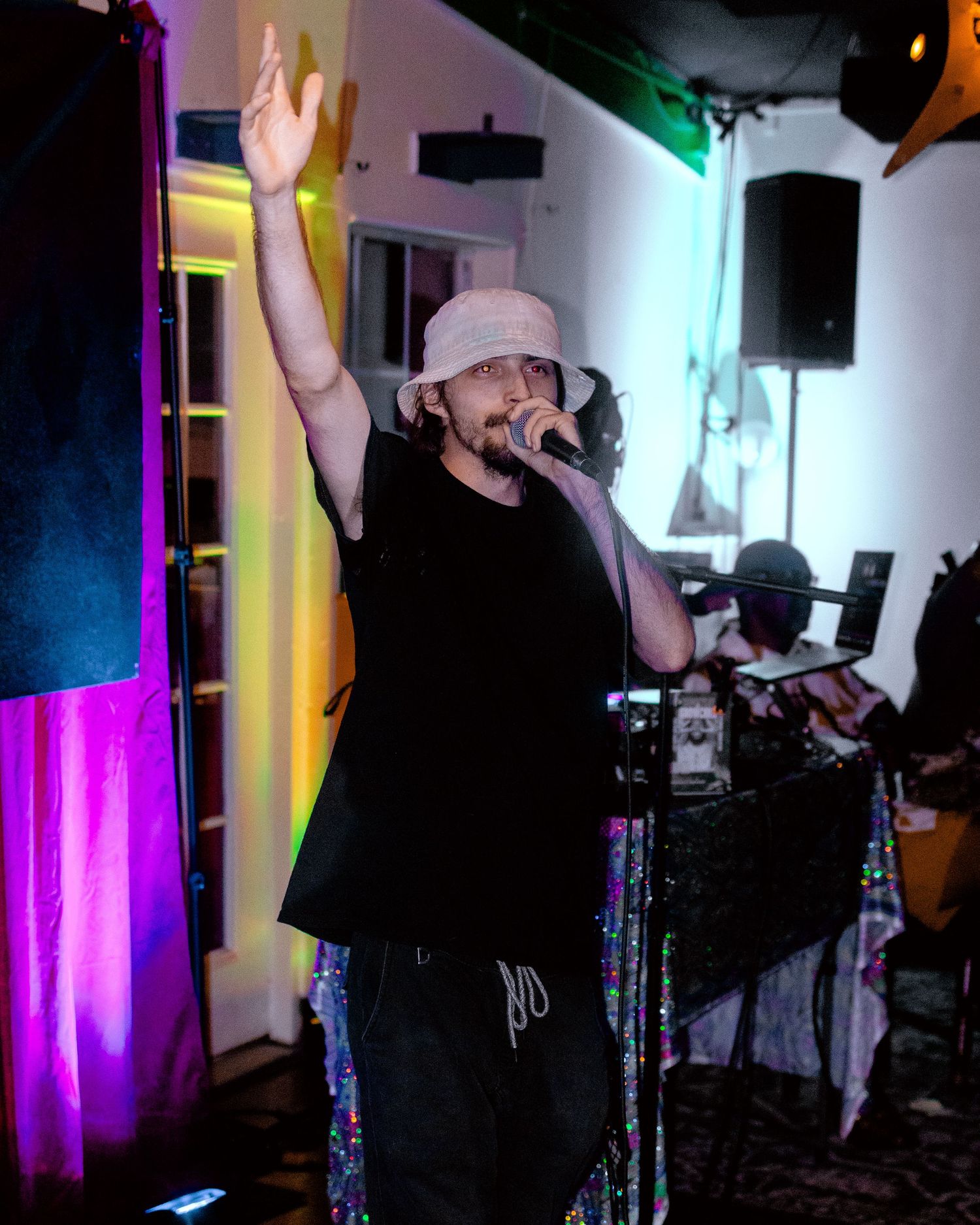 Performer on stage with arms raised under dramatic colored lighting during live show.