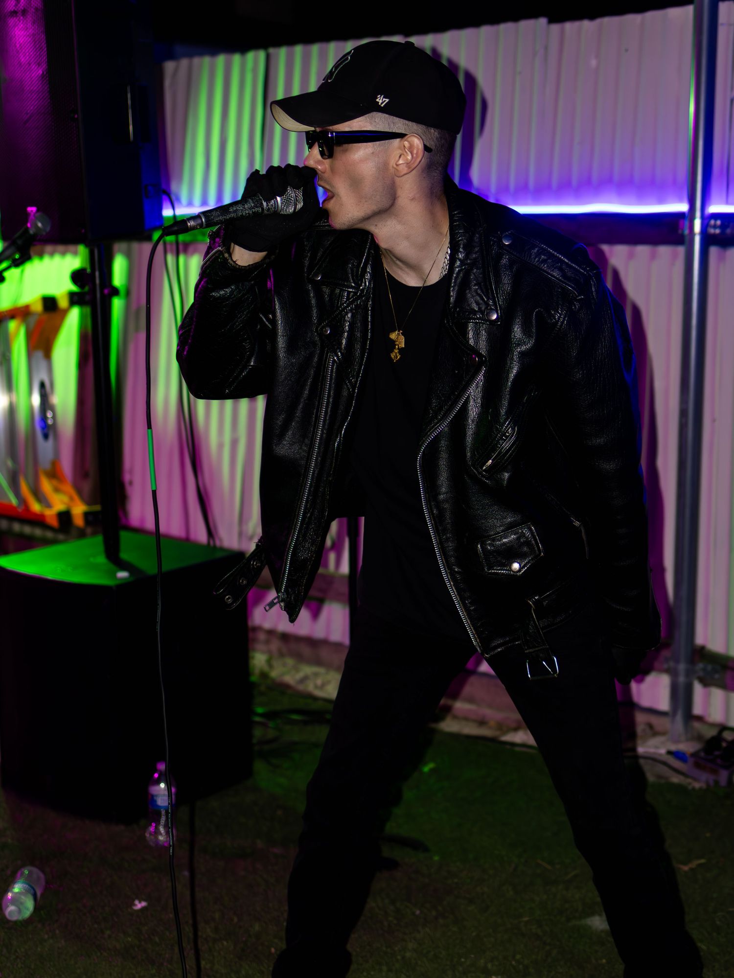 Singer in dark attire performs energetically against purple and green lit backdrop.